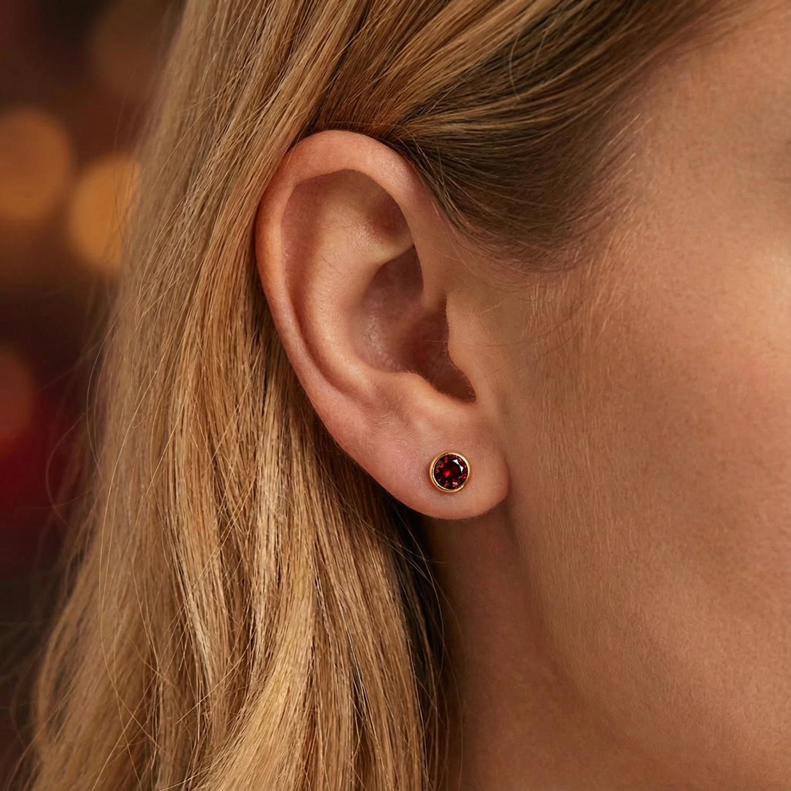 Close-up of a red simulated garnet stud earring in 18K gold vermeil worn on a woman's ear.