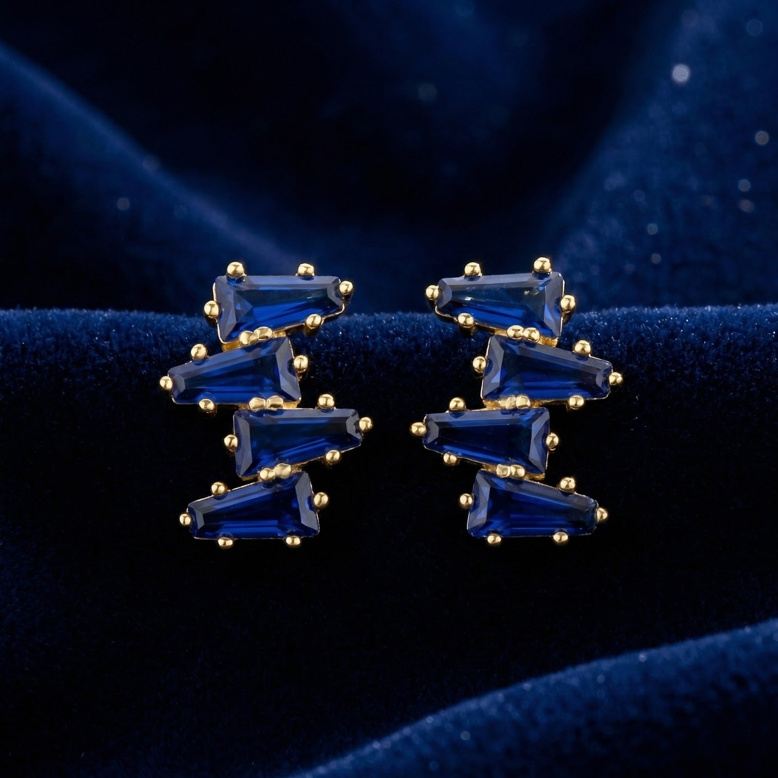 Front view of Vesperis 18K gold vermeil earrings with deep blue simulated sapphire clusters on velvet.