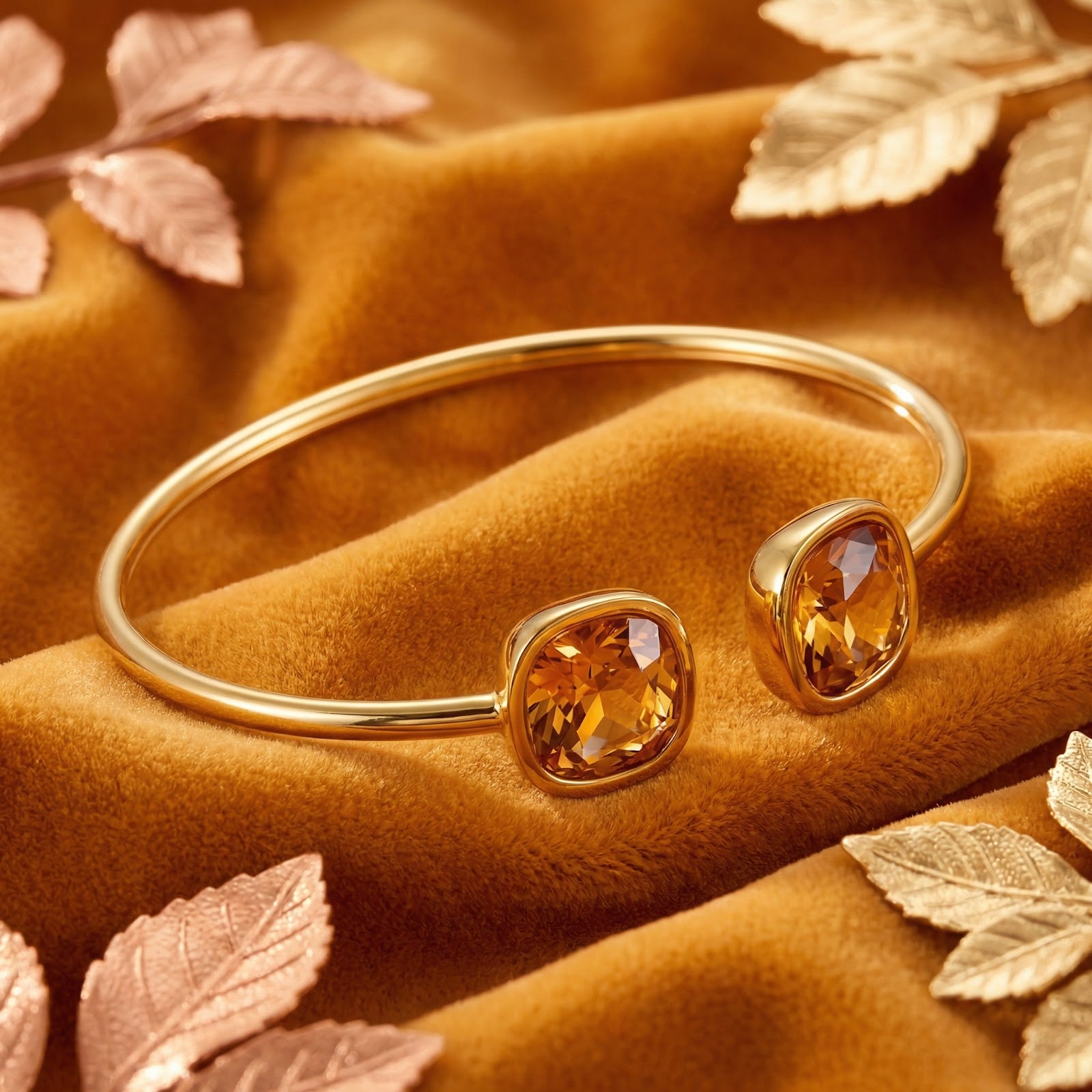 Gold-tone stainless steel Hesperian bangle with cushion-cut simulated topaz stones on orange velvet with autumn leaves.
