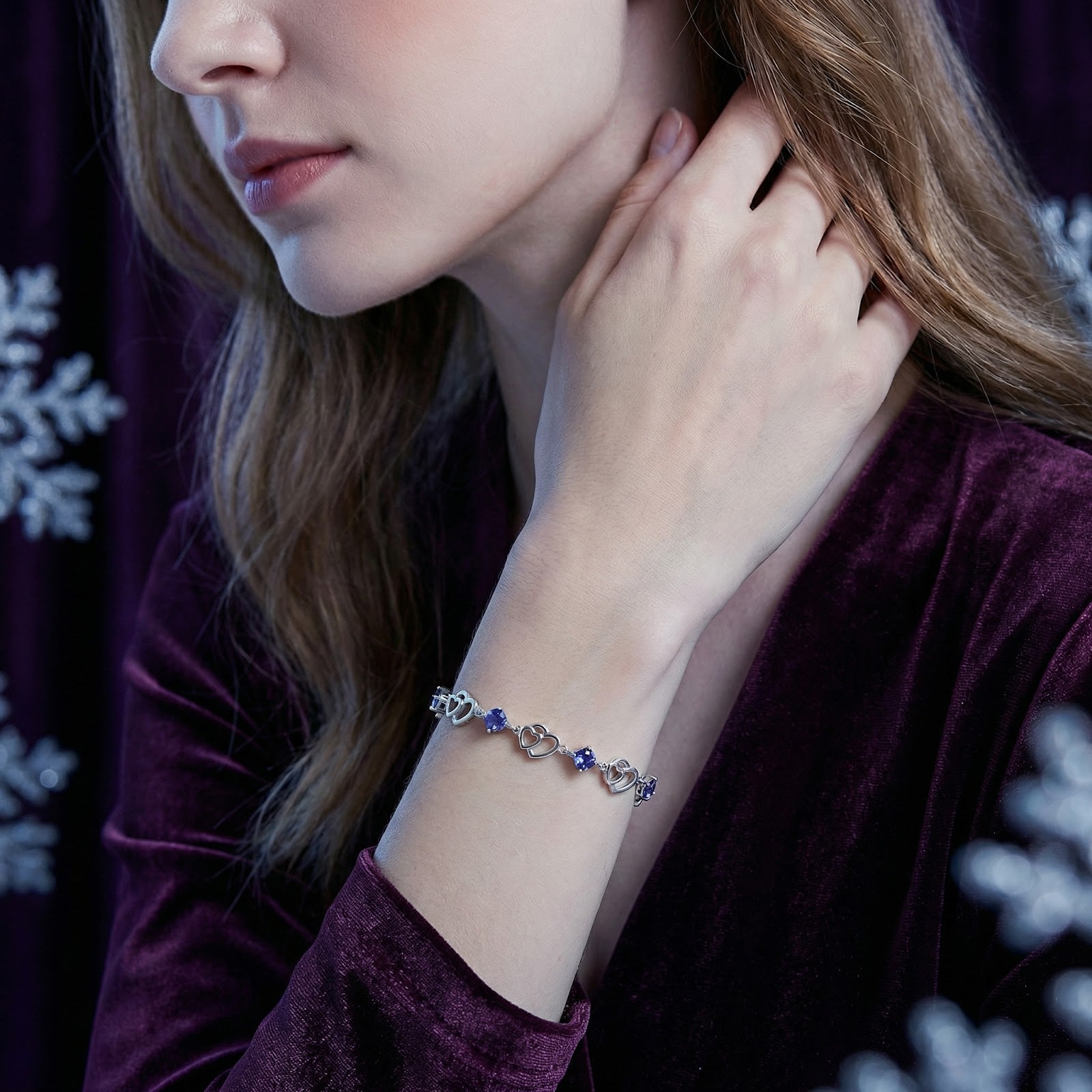 Woman wearing the S925 sterling silver heart-linked bracelet with blue simulated tanzanite stones on her wrist.