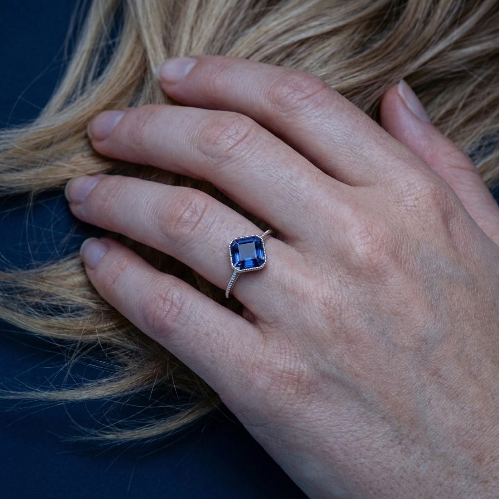 Sterling silver adjustable ring with a square blue sapphire worn on a woman's hand.