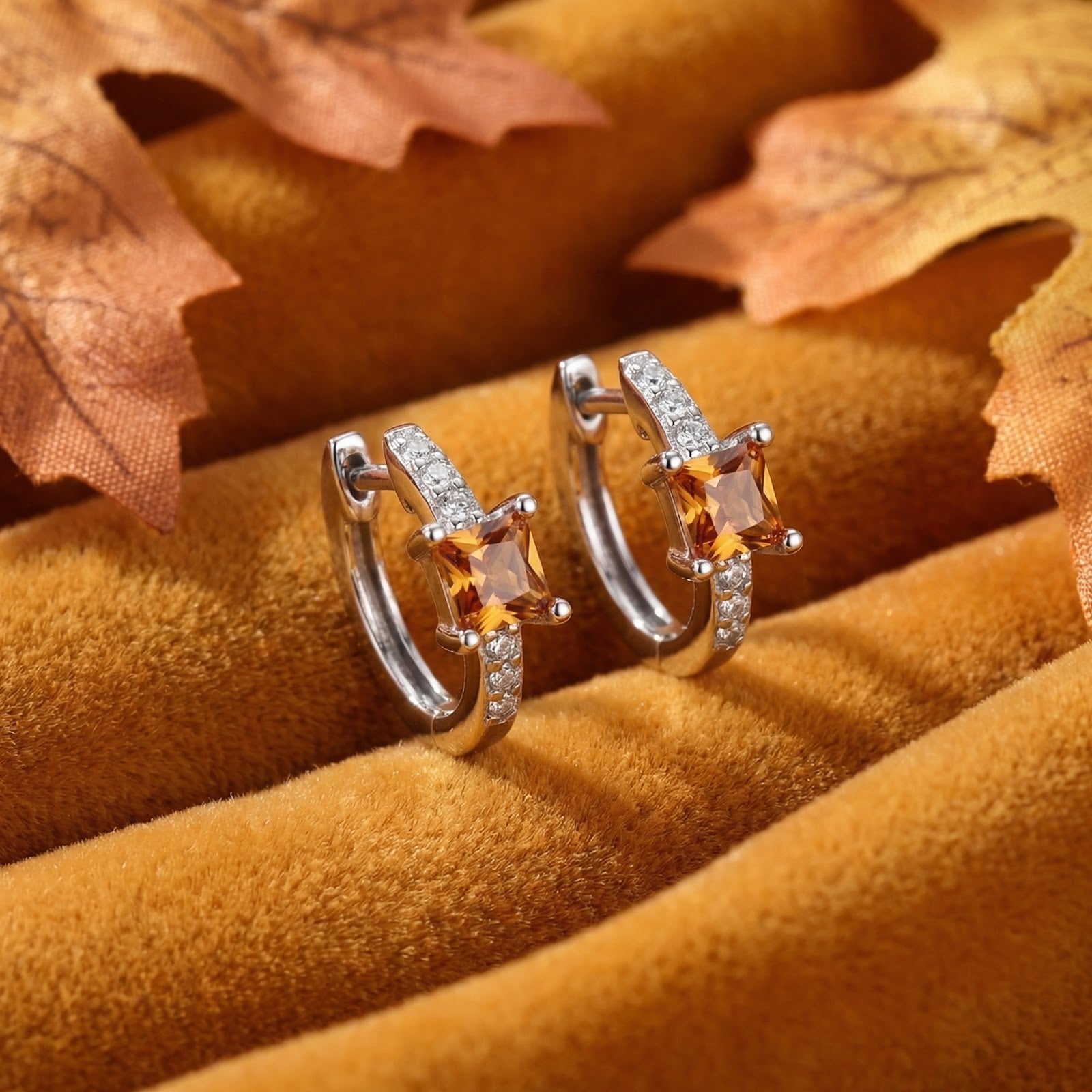 Sterling silver huggie earrings with square-cut orange simulated topaz on golden fabric with autumn leaves.