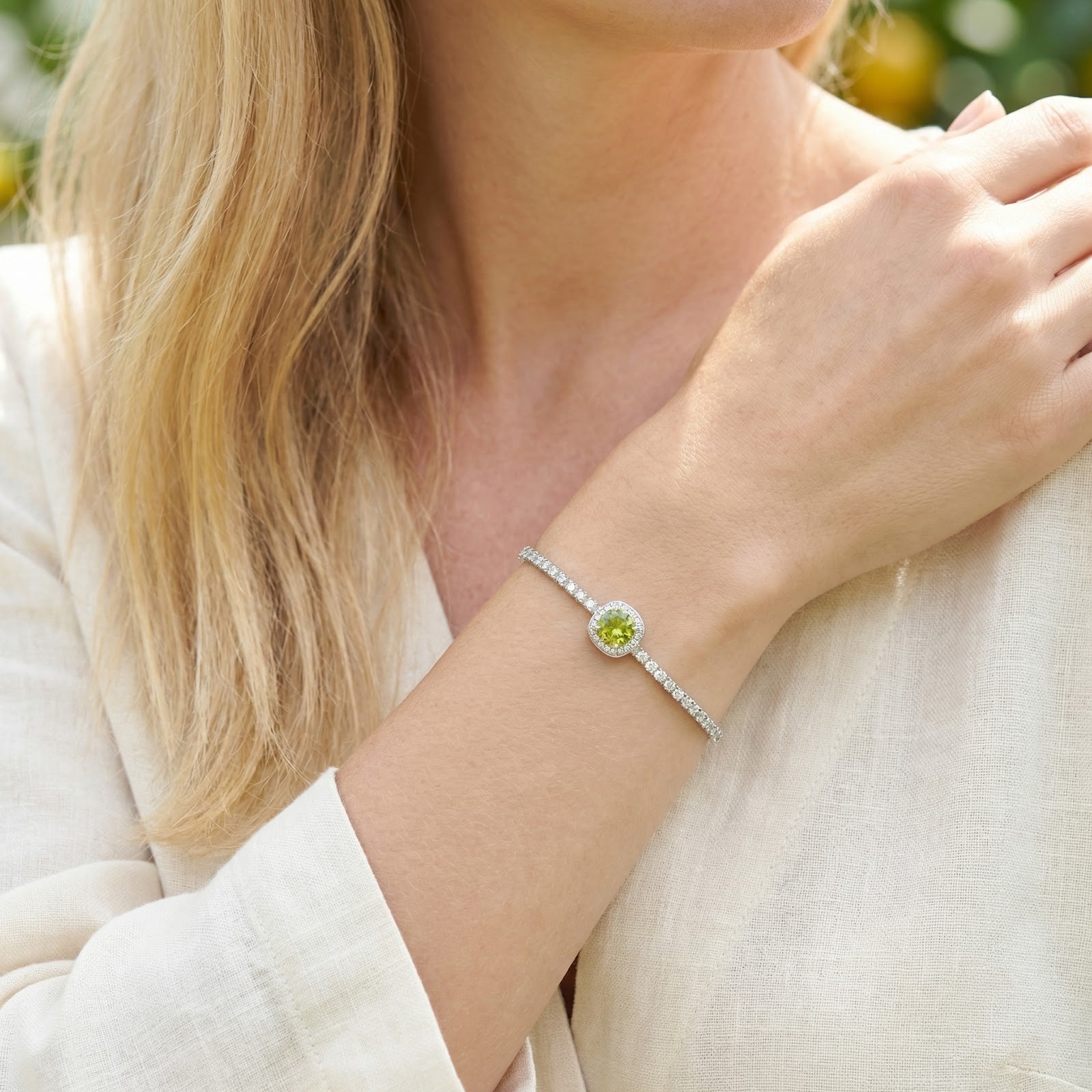 Sterling silver August birthstone bracelet with a round peridot stone worn on a woman's wrist in natural light.