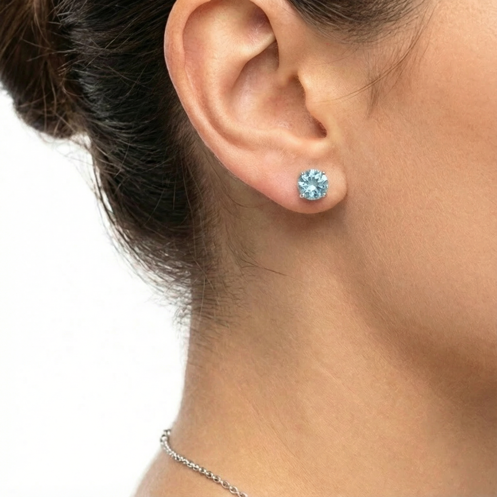 Close-up of a round cut simulated aquamarine sterling silver stud earring worn on a woman's ear.