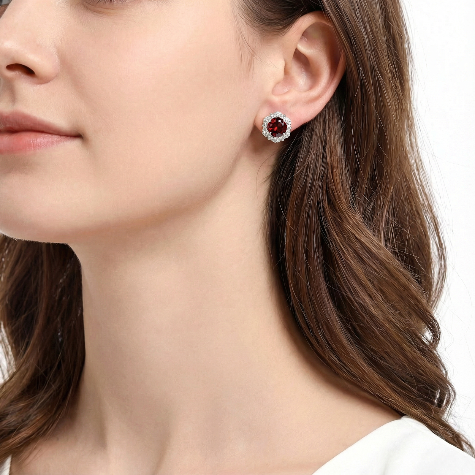 Side view of a woman wearing a round red simulated garnet halo stud earring in sterling silver.