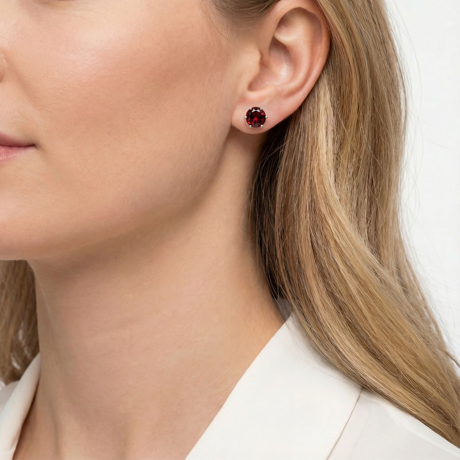 Close-up of a round red garnet stud earring in a silver prong setting worn on a model's ear.