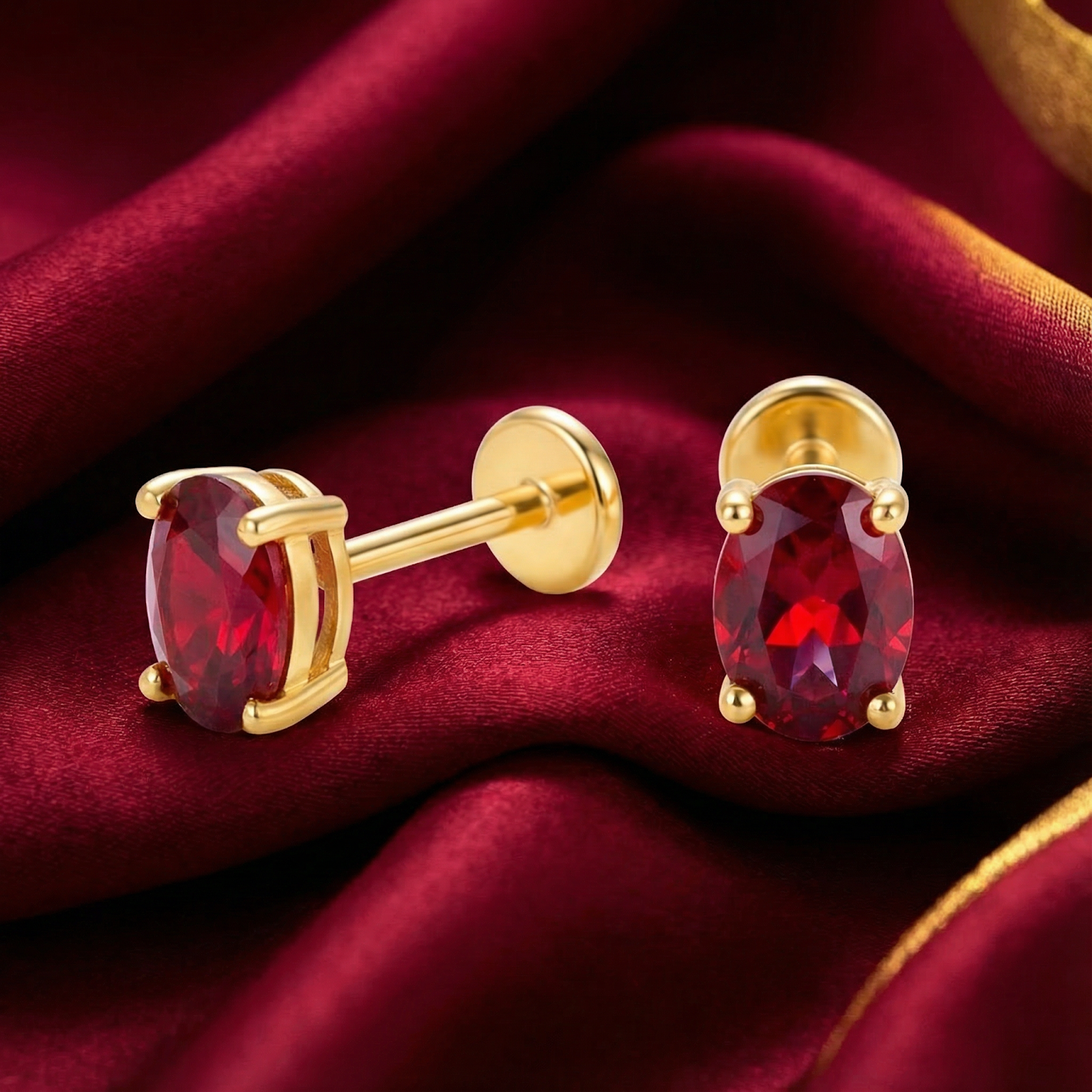 Oval simulated ruby stud earrings in 18K gold vermeil showing front and side views on red silk.