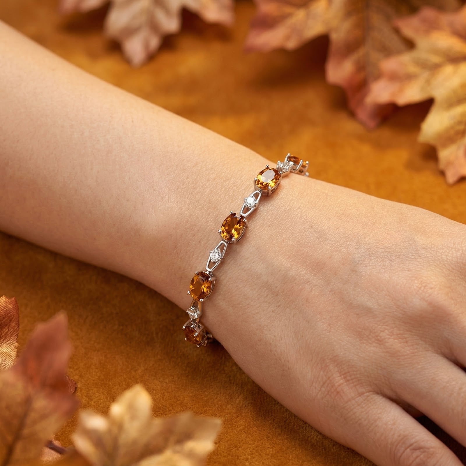 Sterling silver bracelet with oval honey simulated topaz worn on a wrist against an autumn leaf background.
