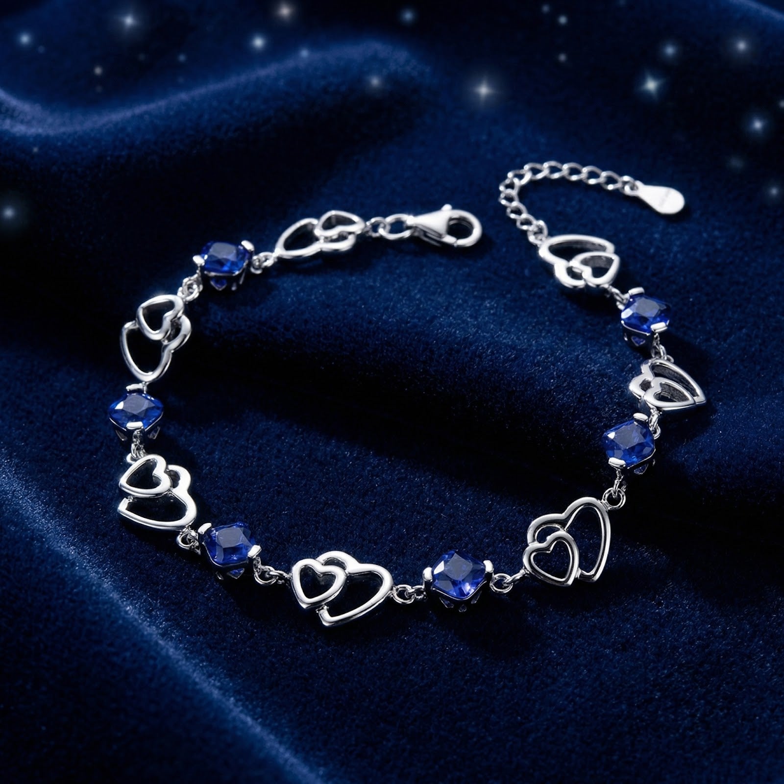 S925 sterling silver Celestelle heart bracelet with square-cut blue simulated sapphires on a starry blue velvet surface.