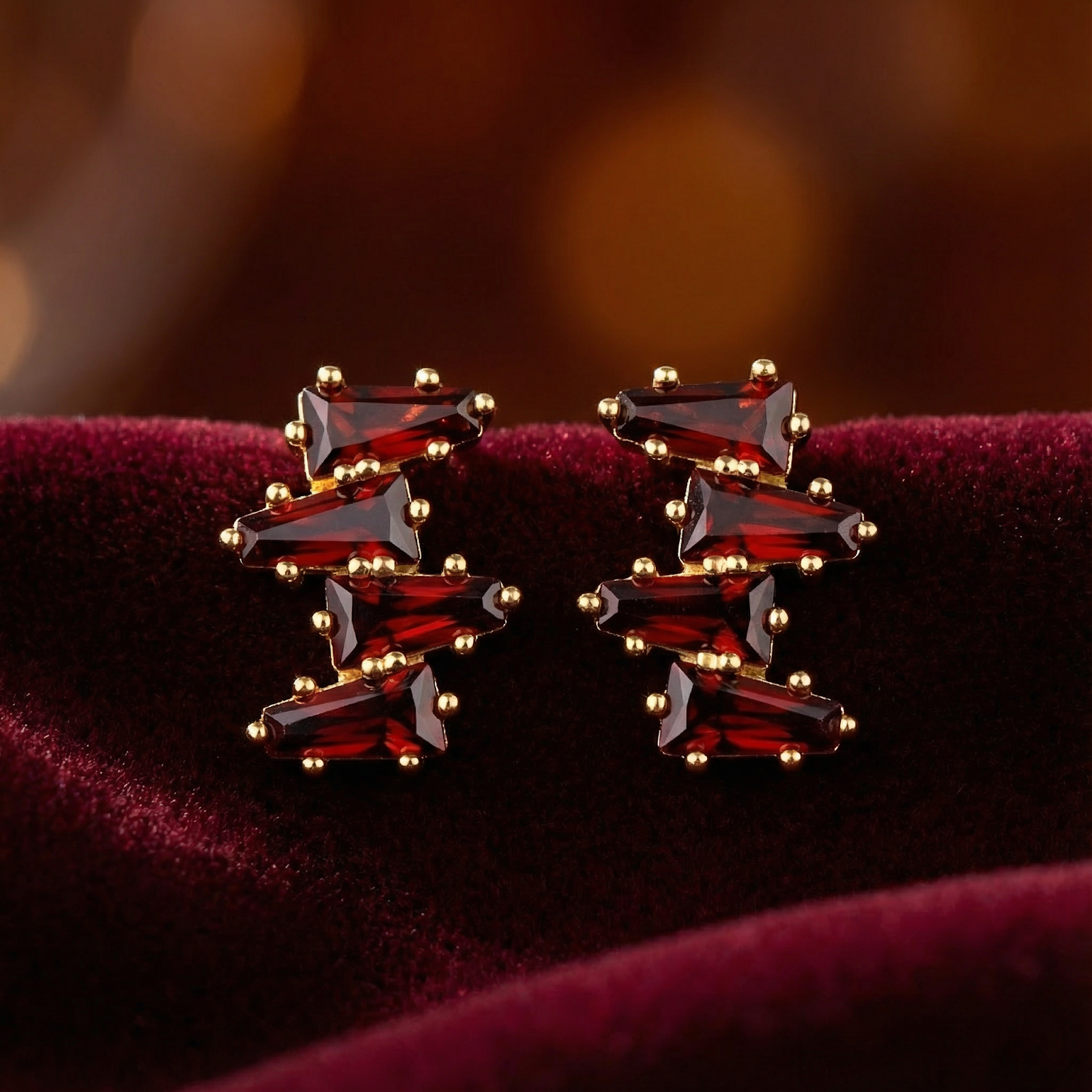 Macro view of red simulated garnet cluster earrings in 18K gold vermeil showing the trapezoid-cut stones.