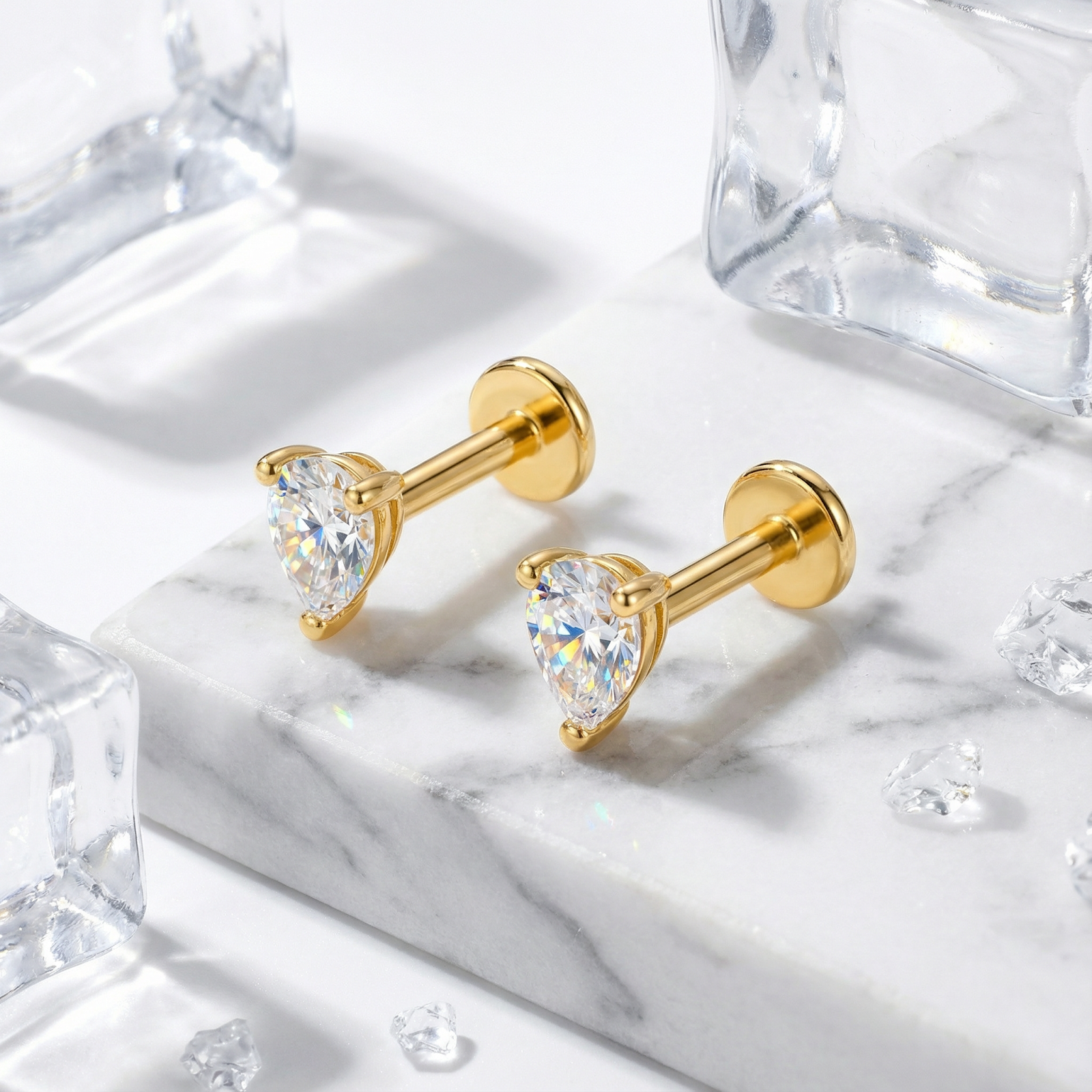 Pear-cut simulated diamond stud earrings in 18K gold vermeil on a marble surface with decorative ice cubes.