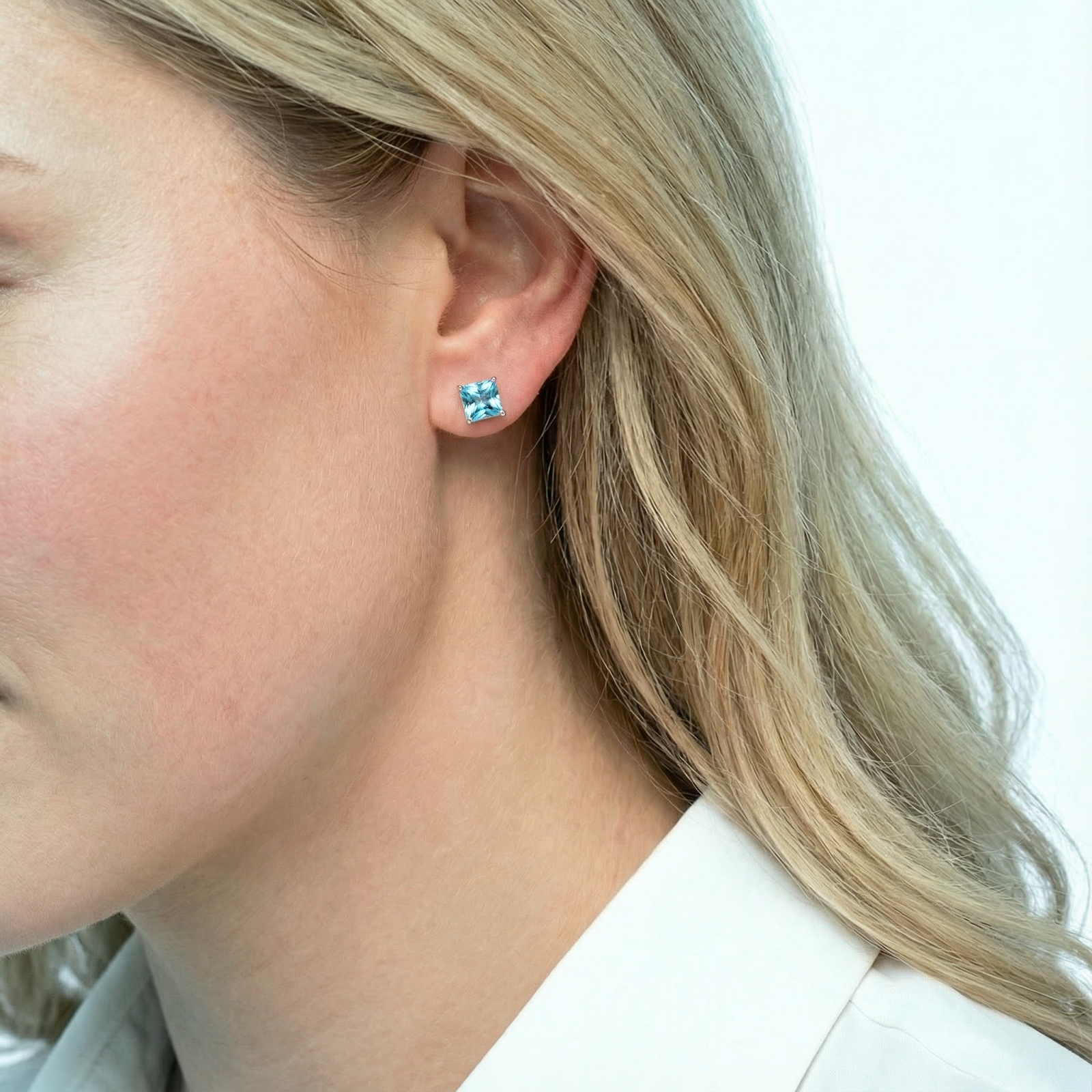 Side profile of a model wearing a princess cut simulated aquamarine stud in 18k rose gold vermeil.