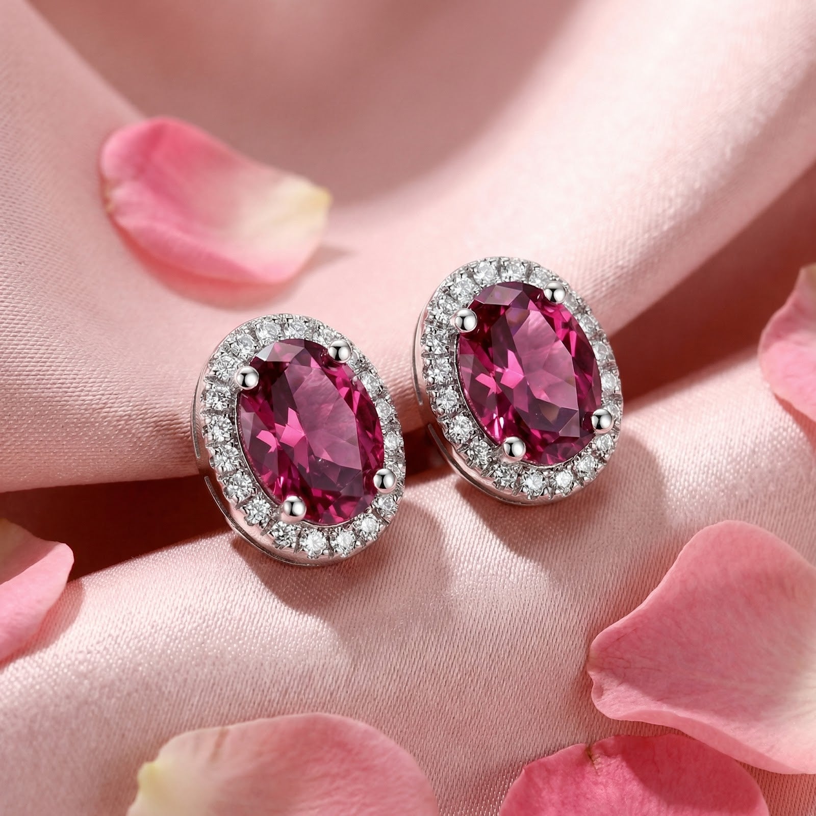 Oval-cut pink tourmaline halo stud earrings in sterling silver displayed on pink silk with rose petals.