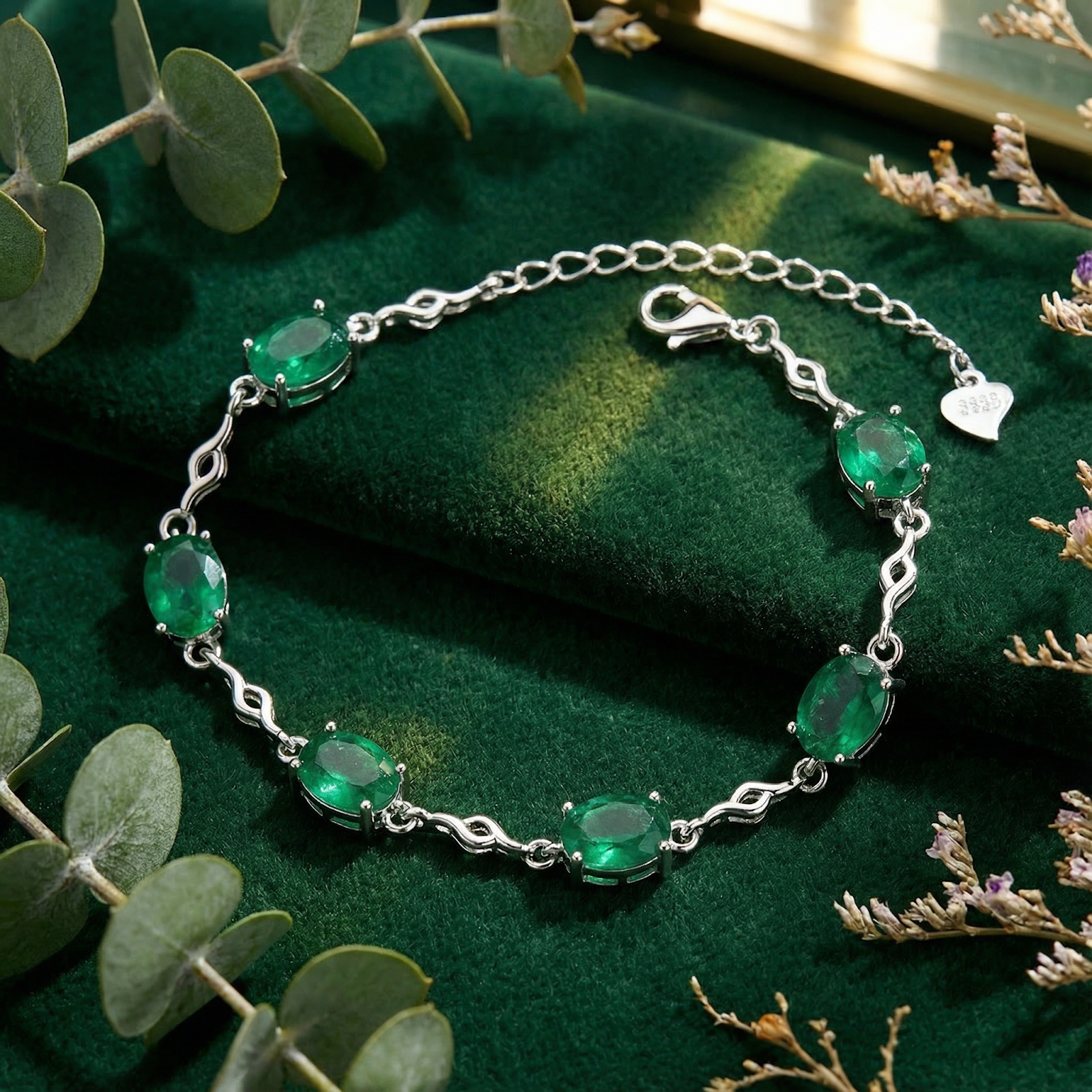 S925 sterling silver station bracelet with oval simulated emeralds on green velvet with eucalyptus leaves.