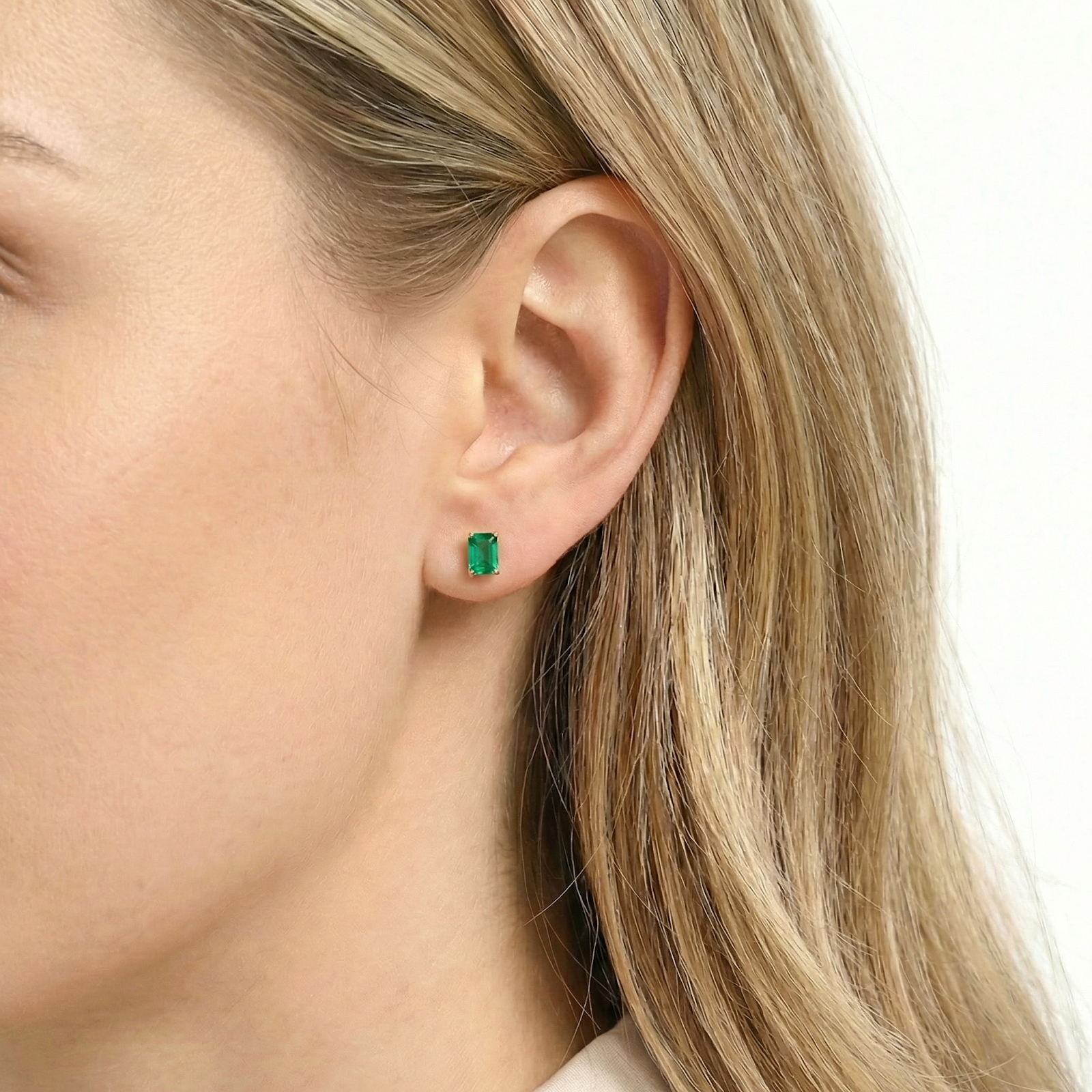 Profile view of a woman wearing an emerald cut simulated emerald stud earring in 18K gold vermeil.