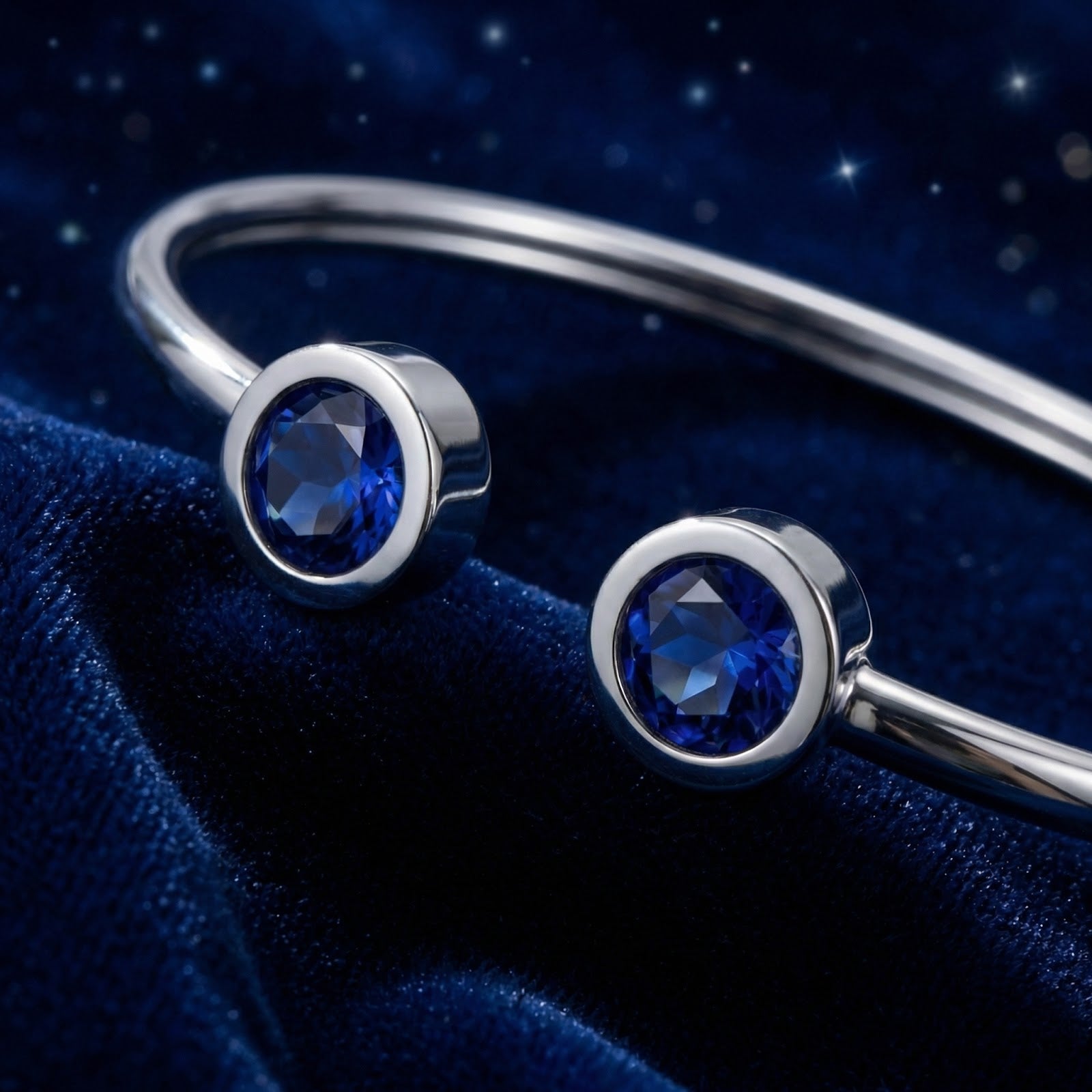 Macro shot of two round-cut blue simulated sapphires in silver stainless steel bezel settings.