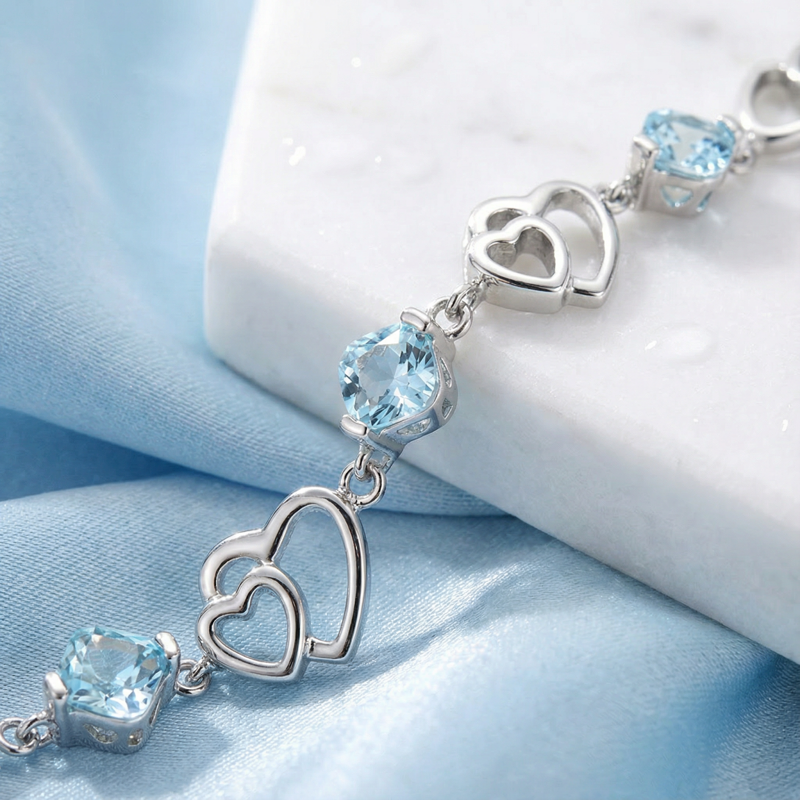 Close-up of sterling silver interlocking heart links and square cut light blue simulated aquamarine stones.