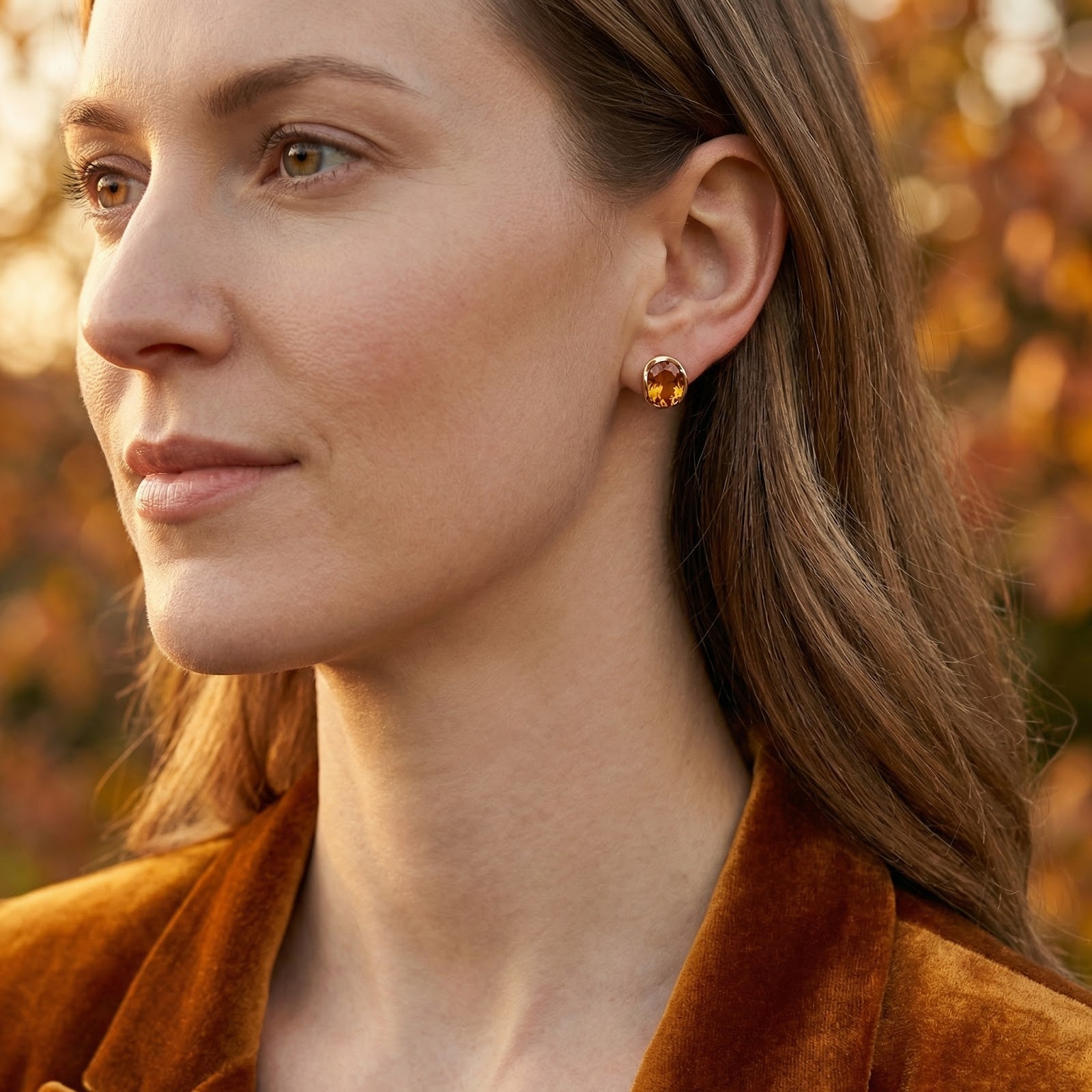 Woman wearing the Caelianna honeyed topaz stud earrings in 18K gold vermeil against an autumn background.