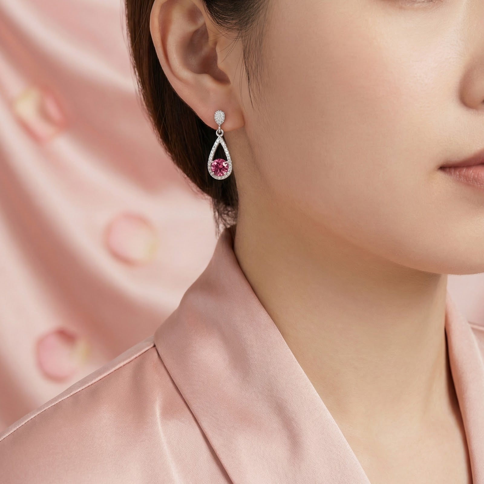 Woman wearing a silver teardrop earring with a round pink tourmaline stone against a pink background.