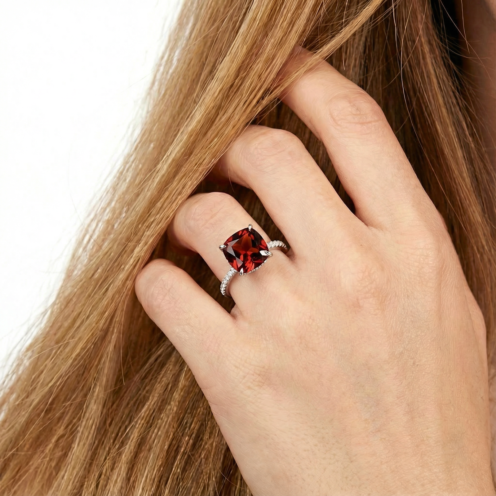 Close-up of a hand wearing the deep red cushion cut garnet ring in sterling silver against blonde hair.