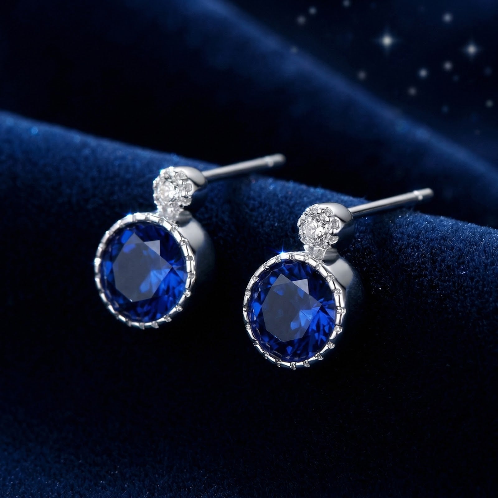 Round blue simulated sapphire stud earrings in S925 sterling silver on a dark blue velvet background.