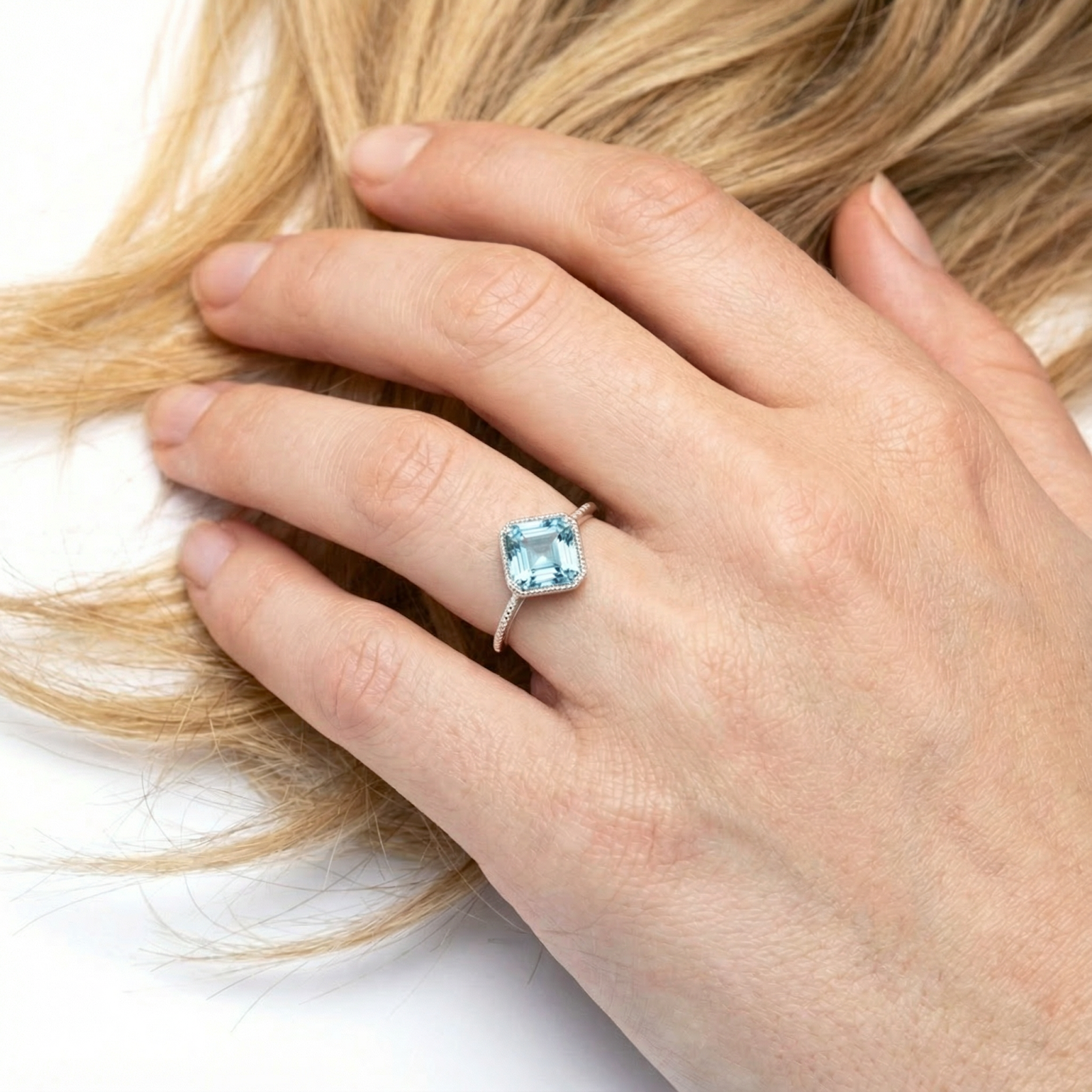 March birthstone simulated aquamarine cushion ring in sterling silver shown on a woman's finger for scale.