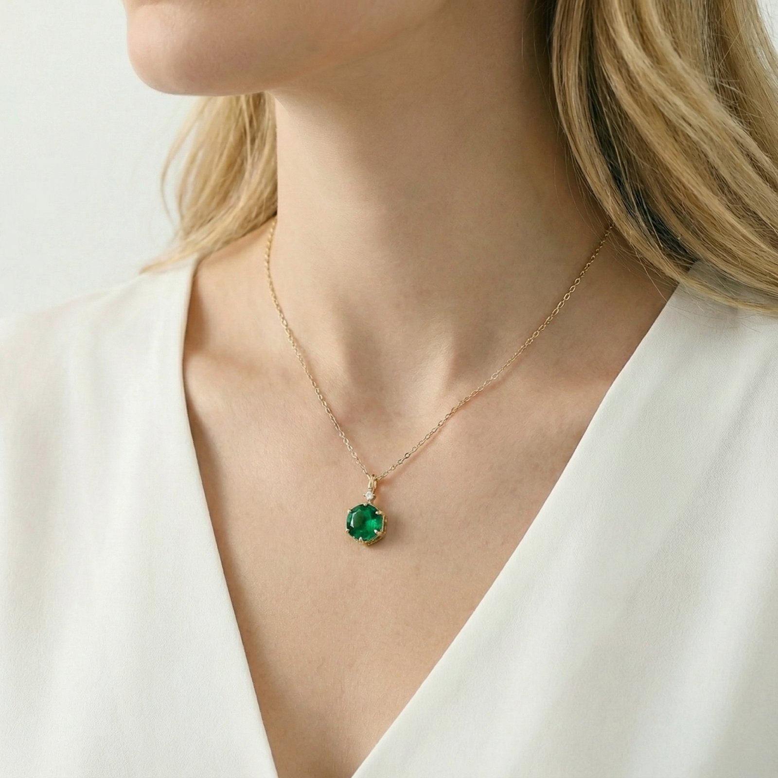 Angled view of a model wearing a round simulated emerald pendant necklace in 18K gold vermeil.