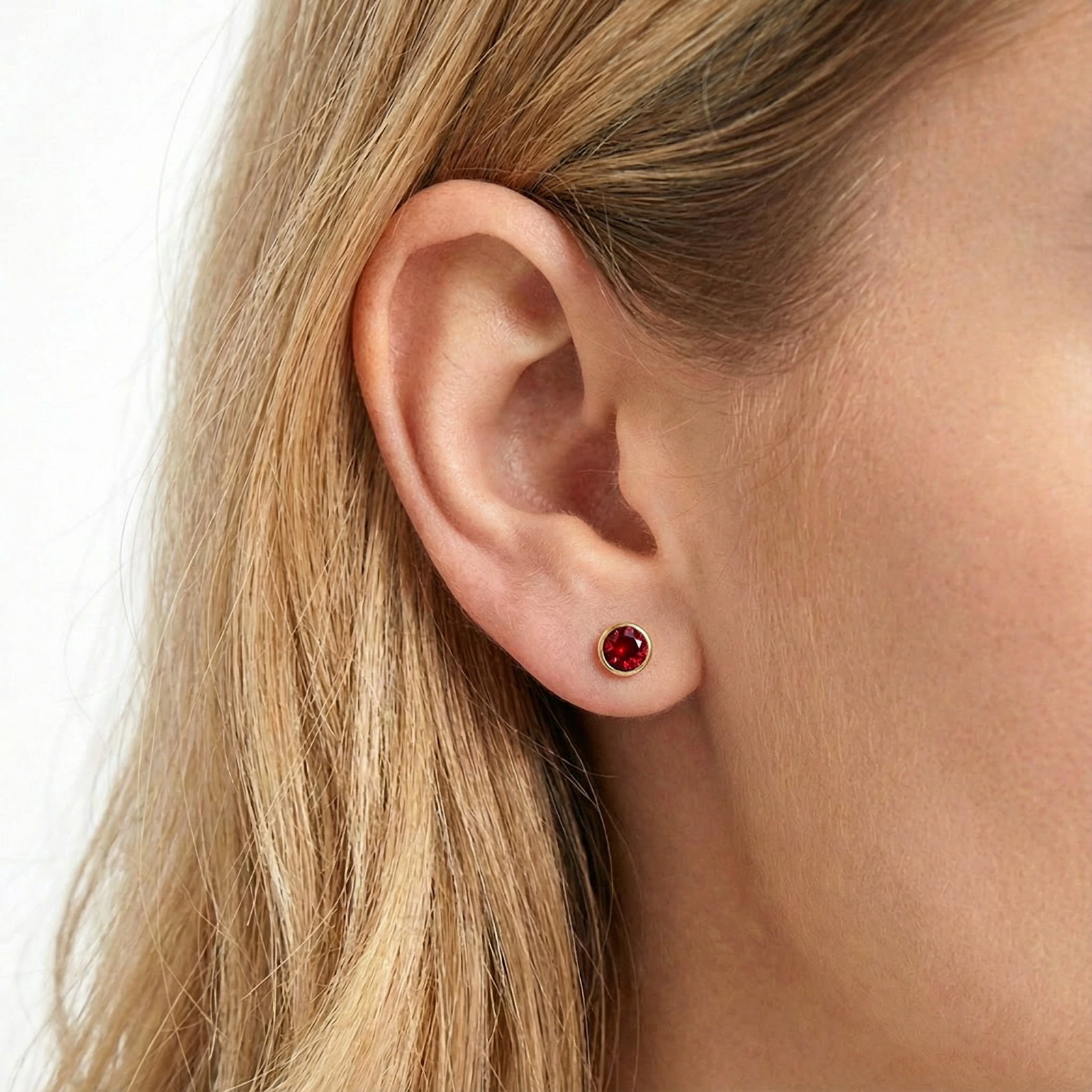 Close-up of a gold vermeil stud earring with a vibrant red simulated ruby on a woman's ear.