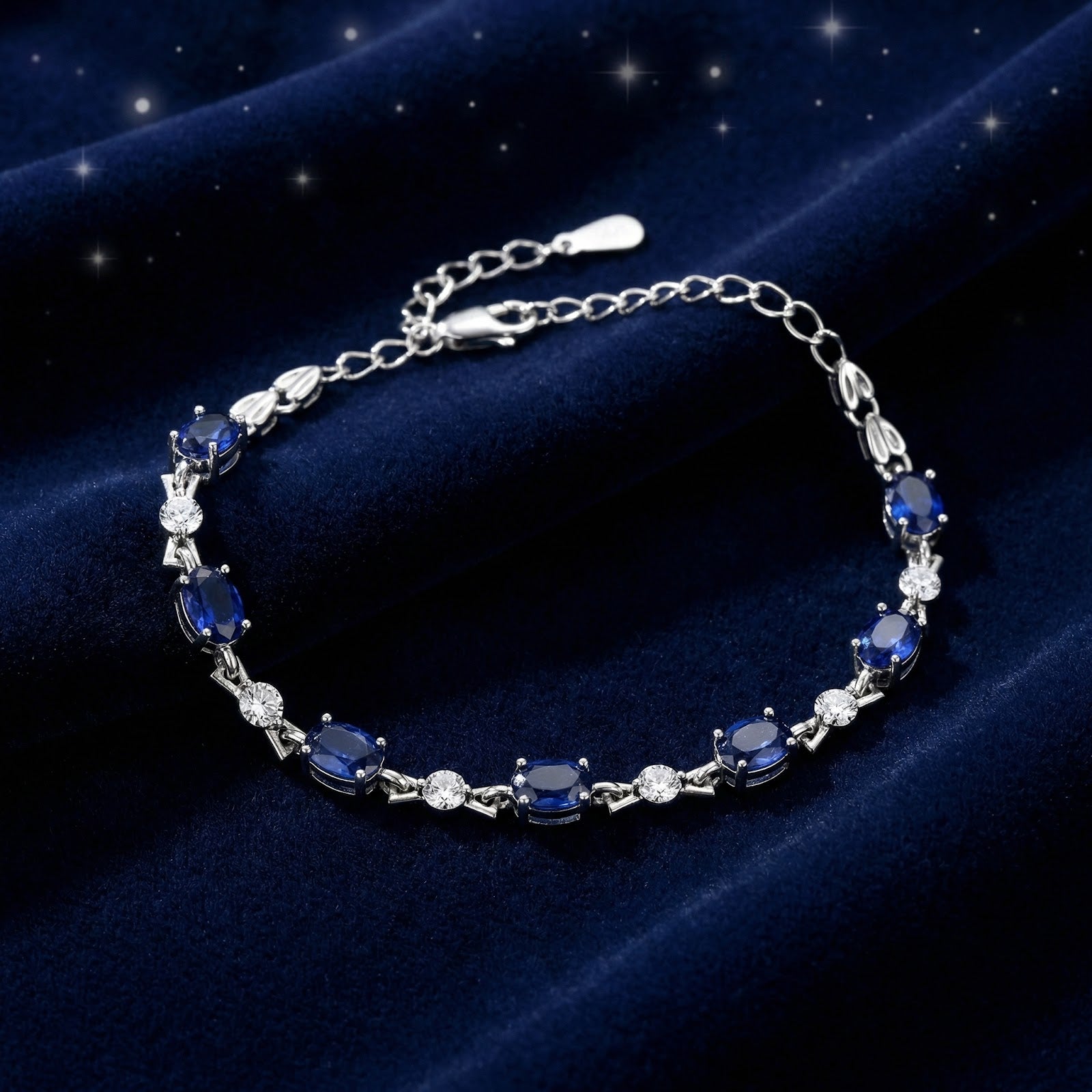 Oval simulated sapphire and sterling silver tennis bracelet on a dark blue velvet background.