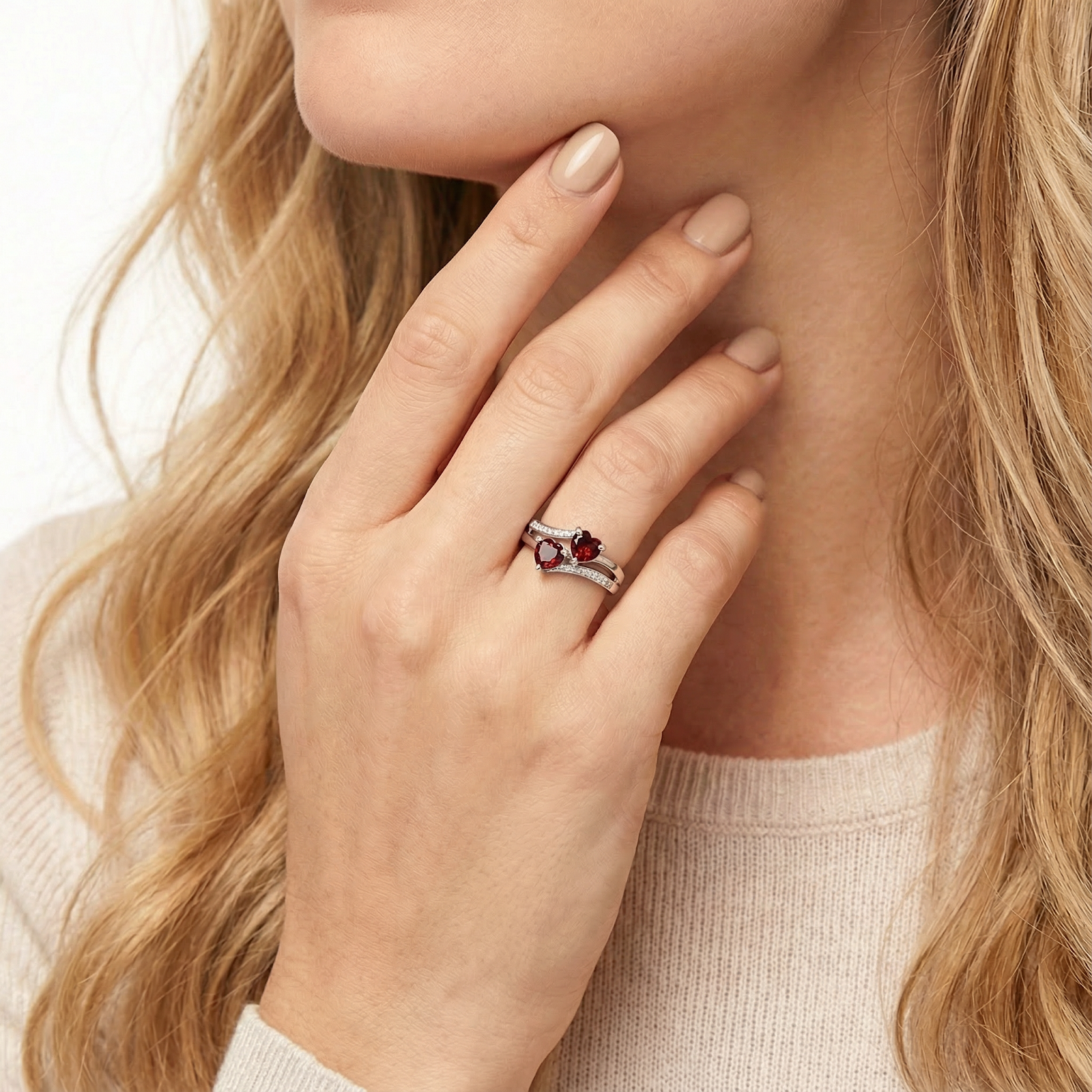 Close-up of a woman's hand wearing a sterling silver ring with two heart cut red simulated garnet stones.