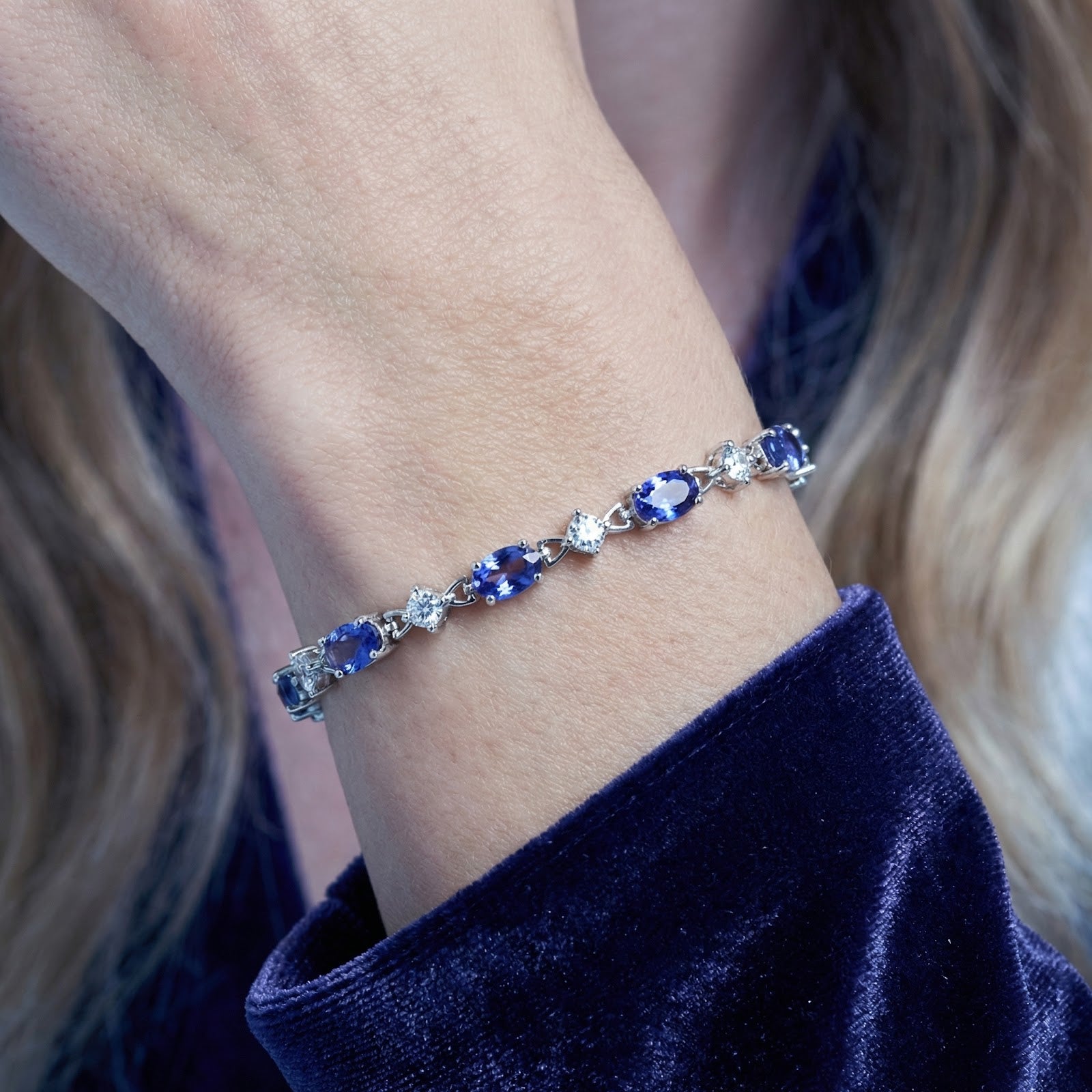 Close-up of oval-cut simulated tanzanite stones in a sterling silver Zenelle station bracelet worn on a wrist.