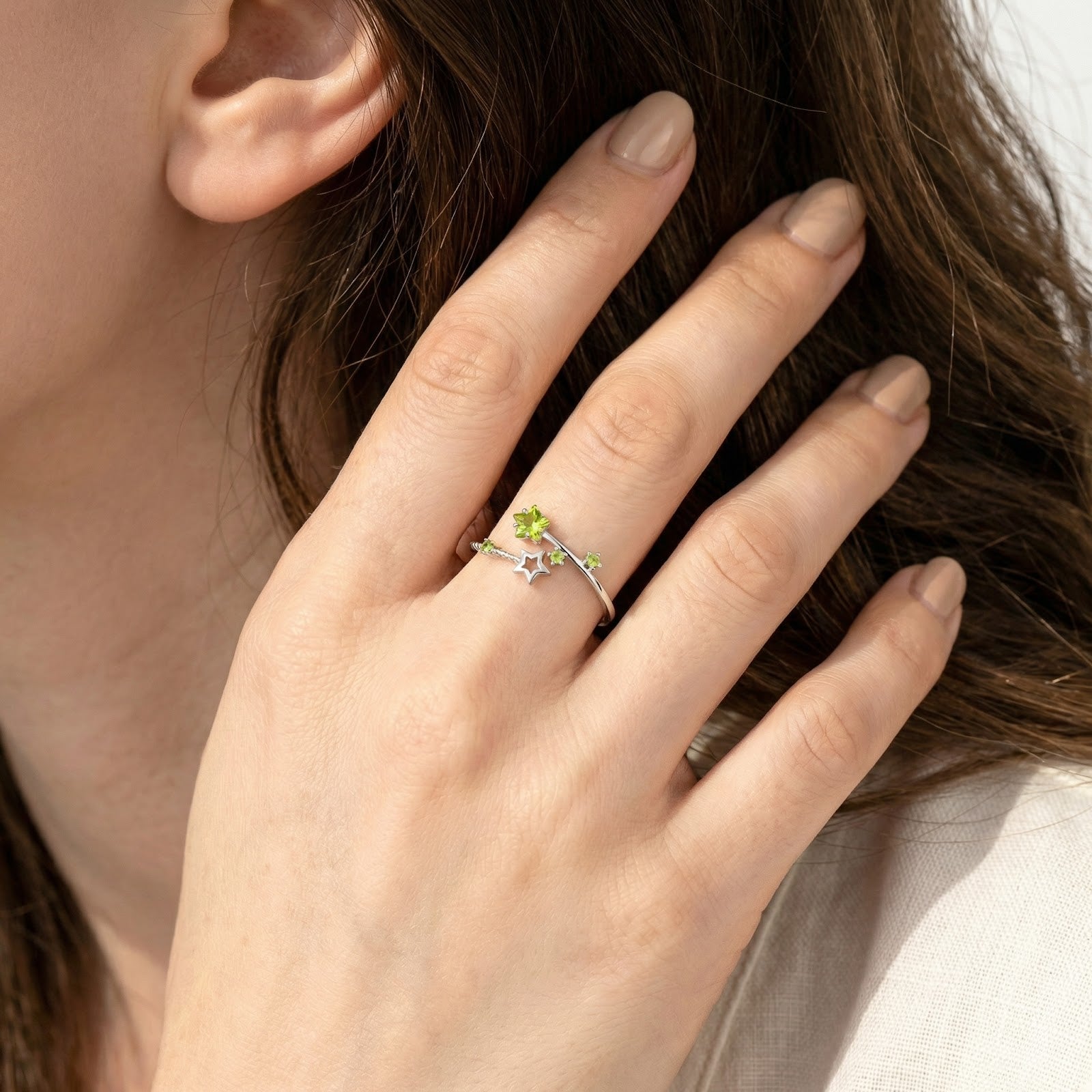 Stellina star bypass ring in sterling silver with simulated peridot worn on a woman's ring finger.