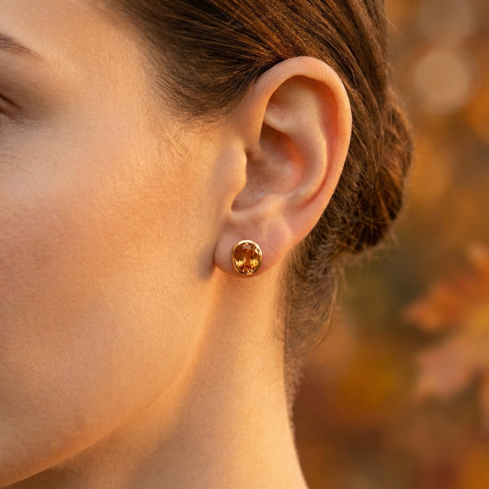 Side view of a woman wearing an oval honeyed simulated topaz stud earring in 18K gold vermeil.