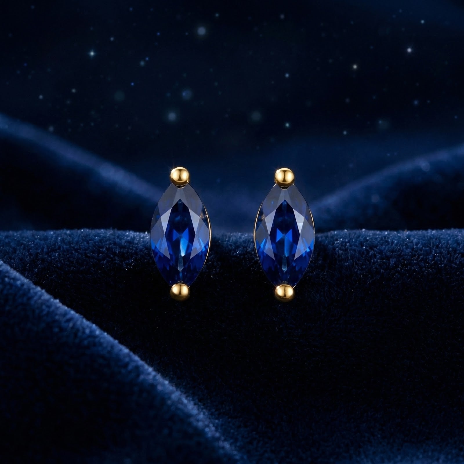 Front view of marquise cut simulated sapphire stud earrings in 18K gold vermeil on a blue velvet background.
