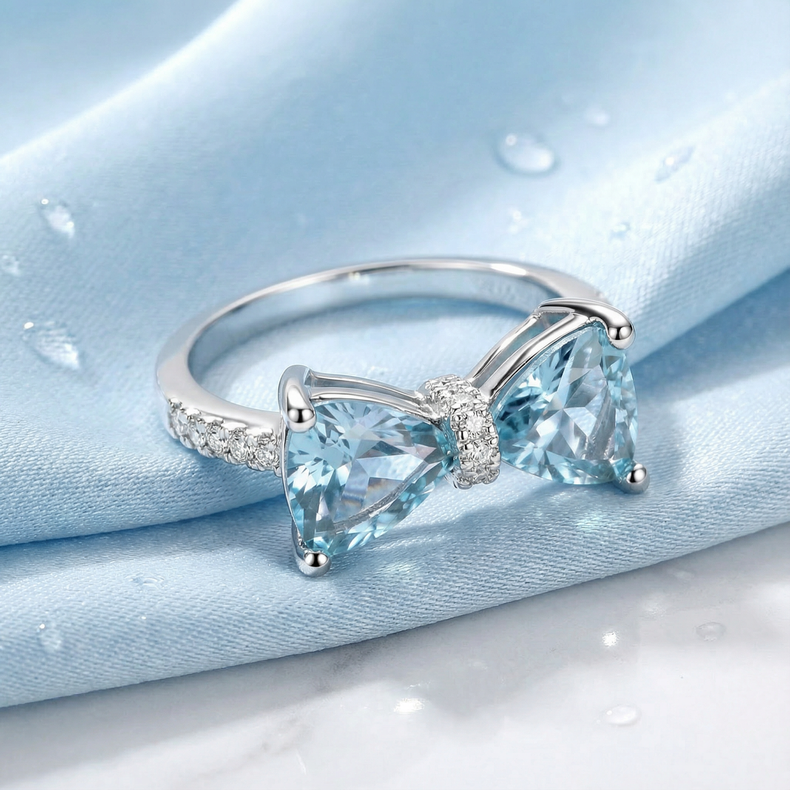 Close-up of a sterling silver bow ring featuring dual trillion-cut light blue simulated aquamarine stones.