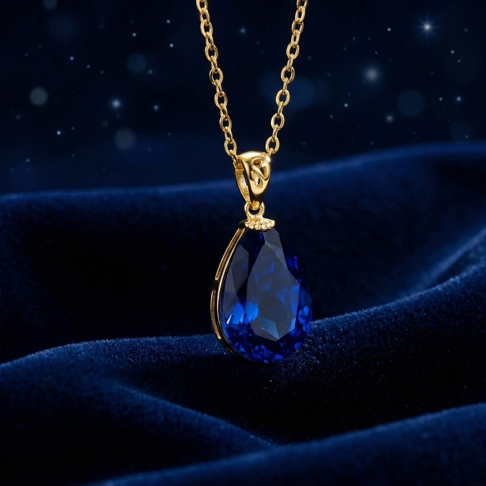 Pear-cut simulated blue sapphire pendant in 18K gold vermeil displayed on textured blue velvet.
