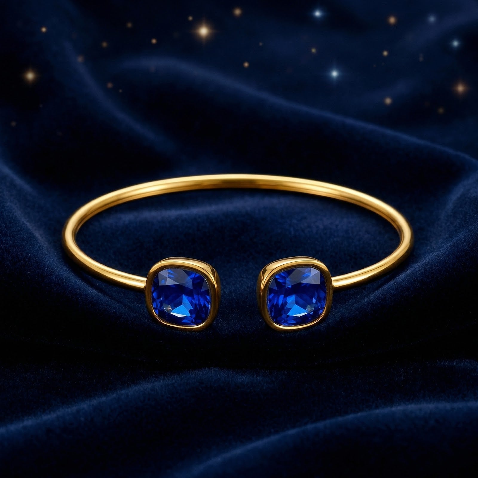Front view of a gold-finish stainless steel cuff with two cushion-cut blue sapphires on velvet.
