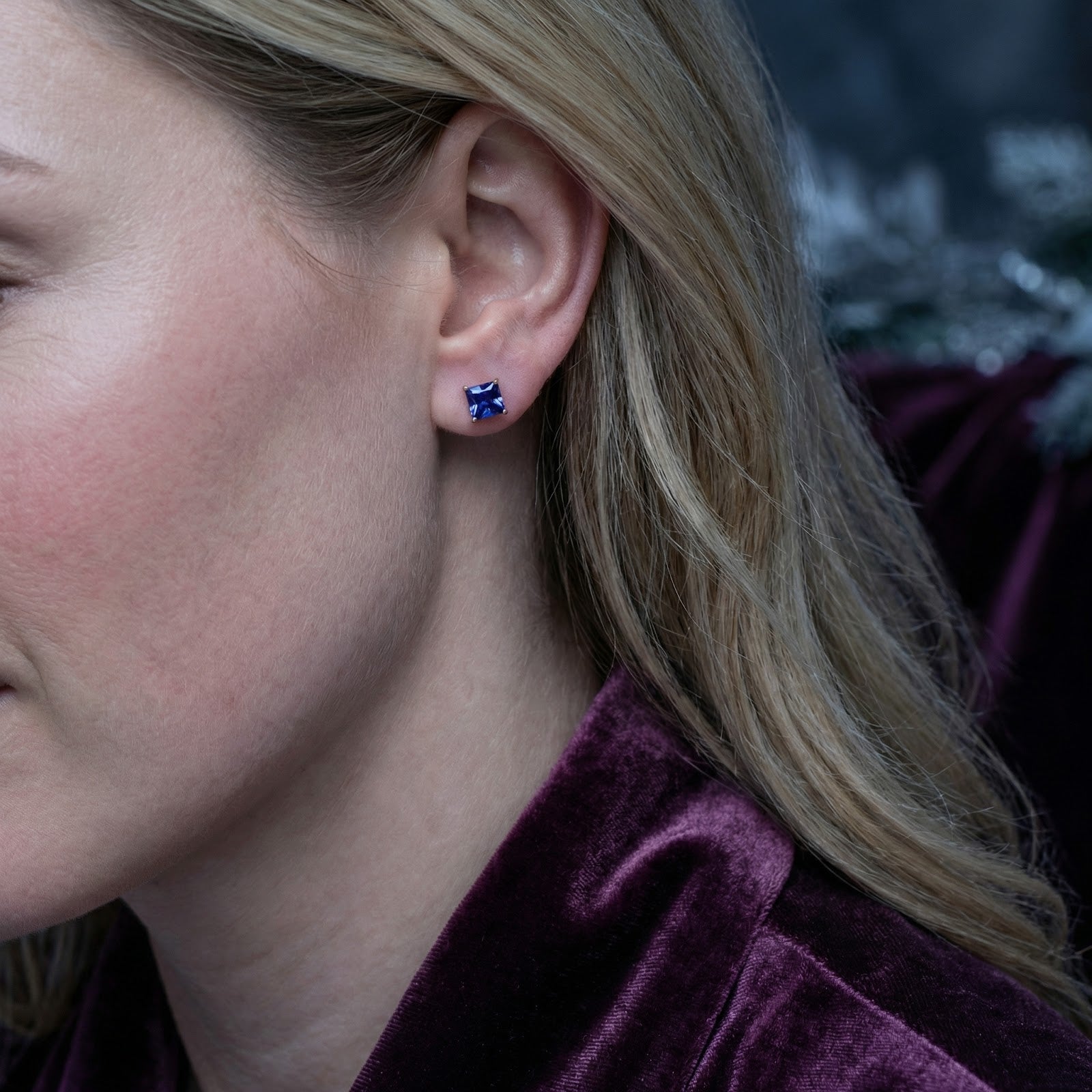 Side view of a woman wearing a blue princess-cut simulated tanzanite stud earring in 18K rose gold vermeil.