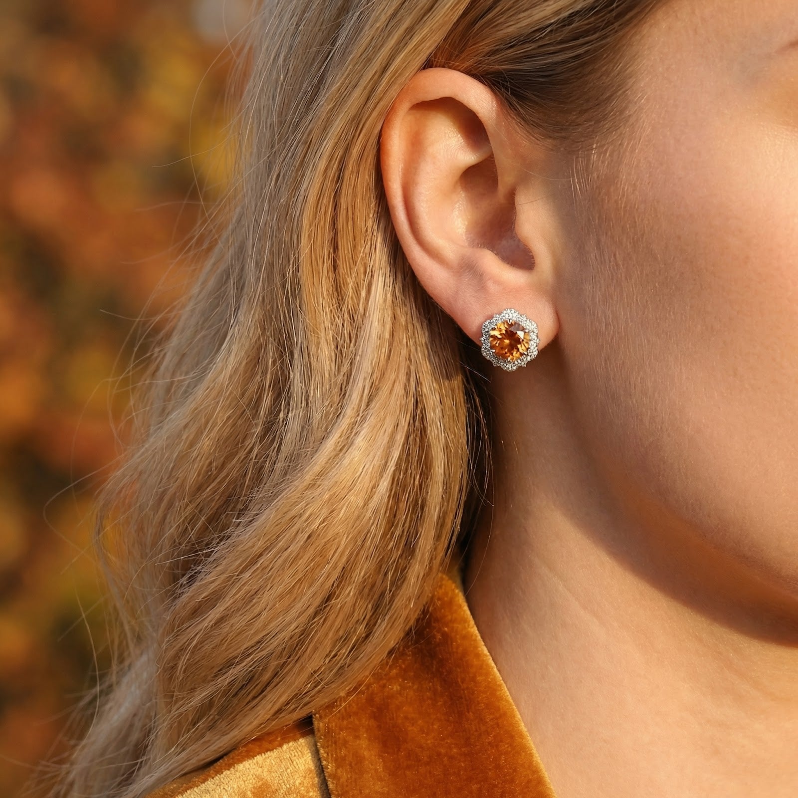 Close-up of a woman wearing a sterling silver halo stud earring featuring a round honey-toned simulated topaz.