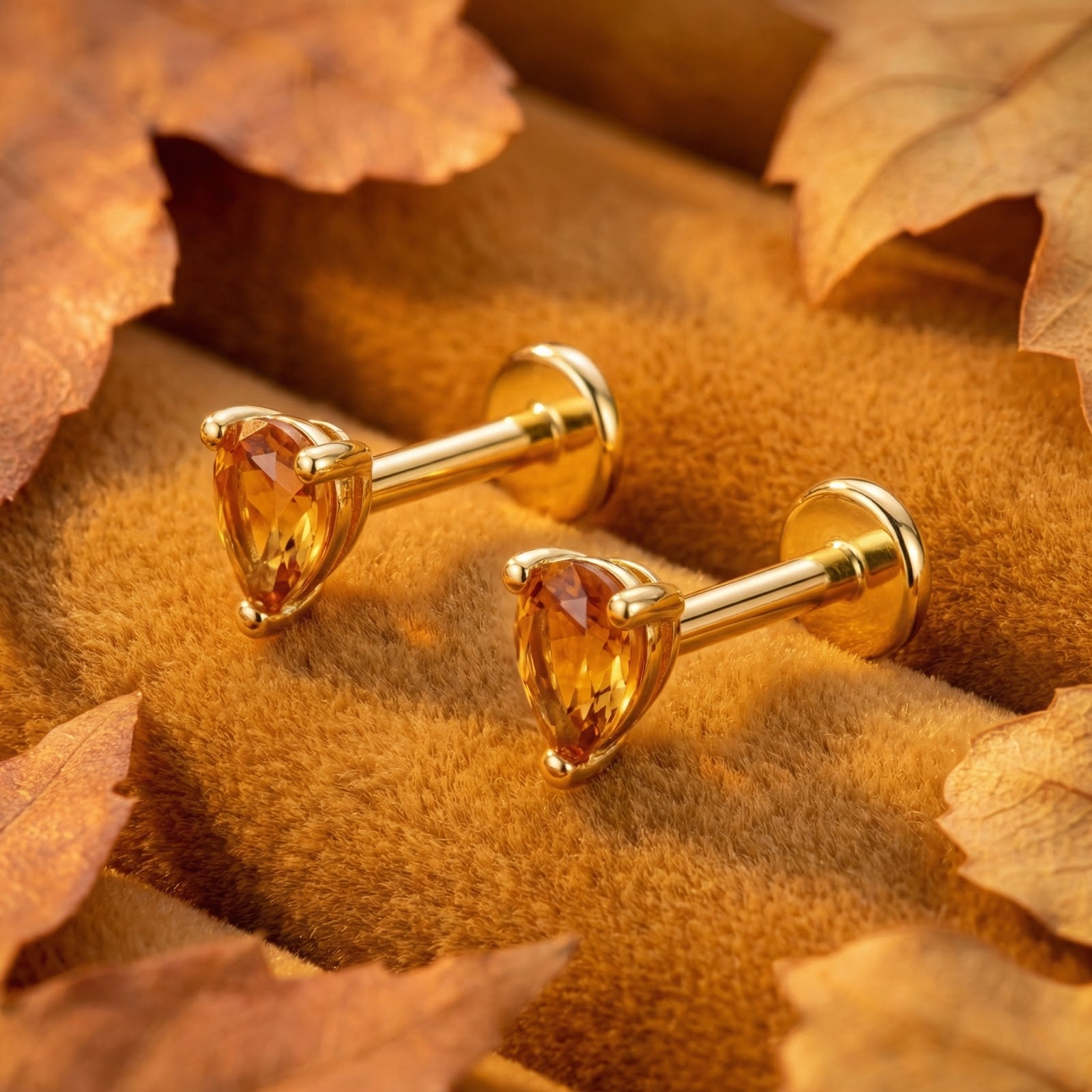 Pear-cut simulated topaz earrings in 18K gold vermeil displayed on brown velvet with autumn leaves.