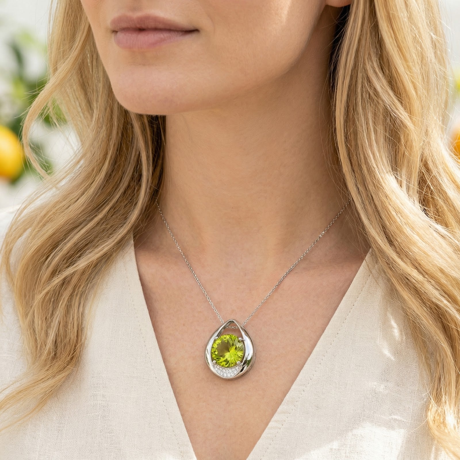 Model wearing the sterling silver teardrop necklace featuring a round simulated peridot and small accent stones.