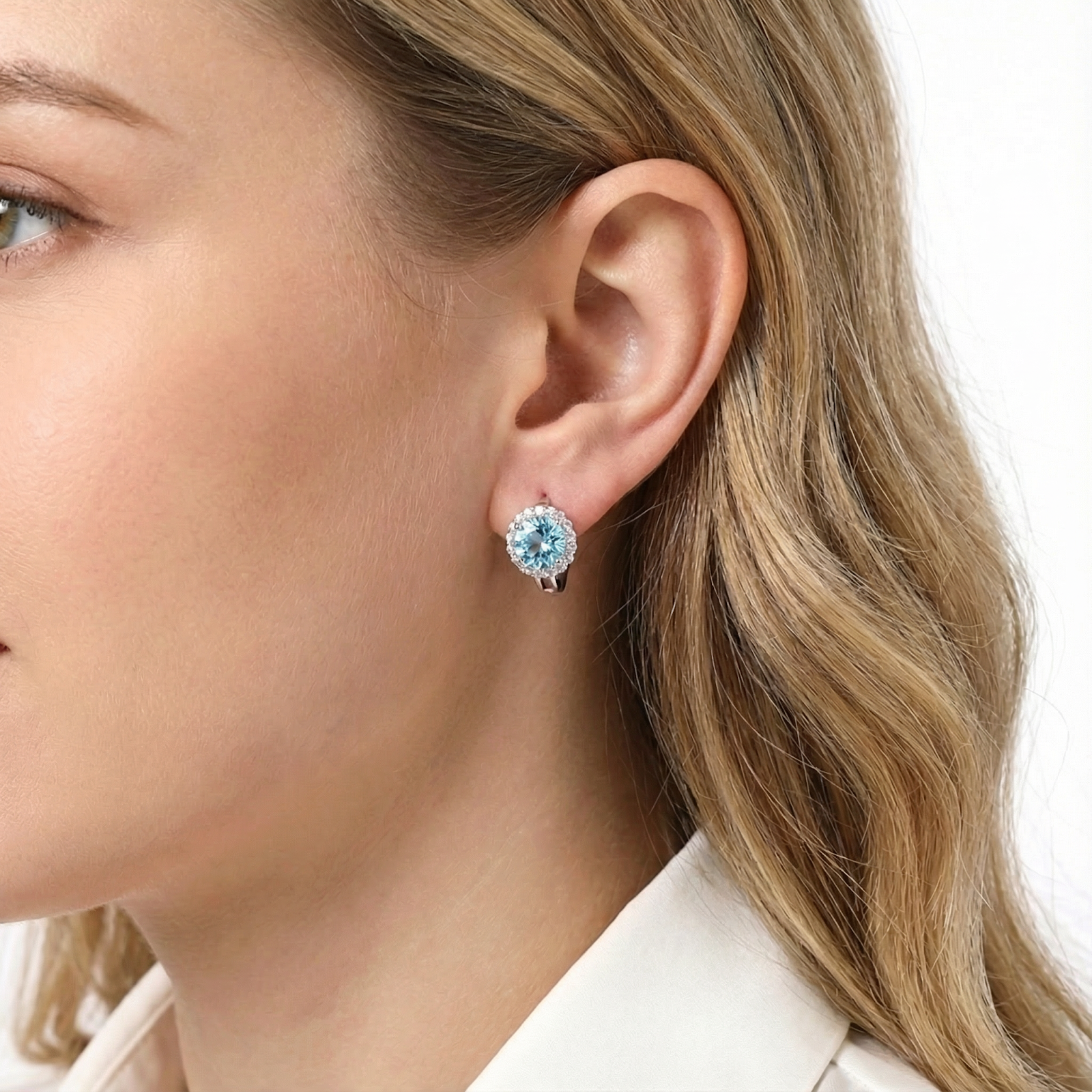 Woman wearing a round cut light blue simulated aquamarine halo drop earring in sterling silver.