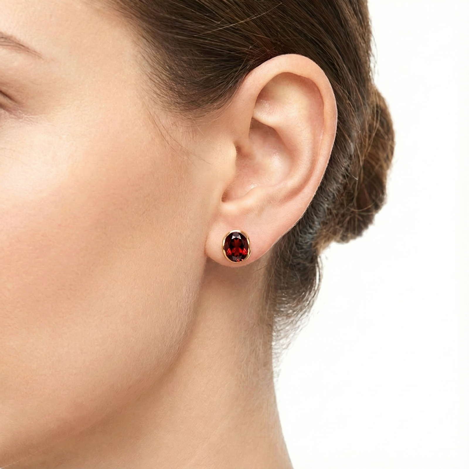 Model wearing the Evelina 18K gold vermeil huggie earring featuring a round cut simulated garnet.