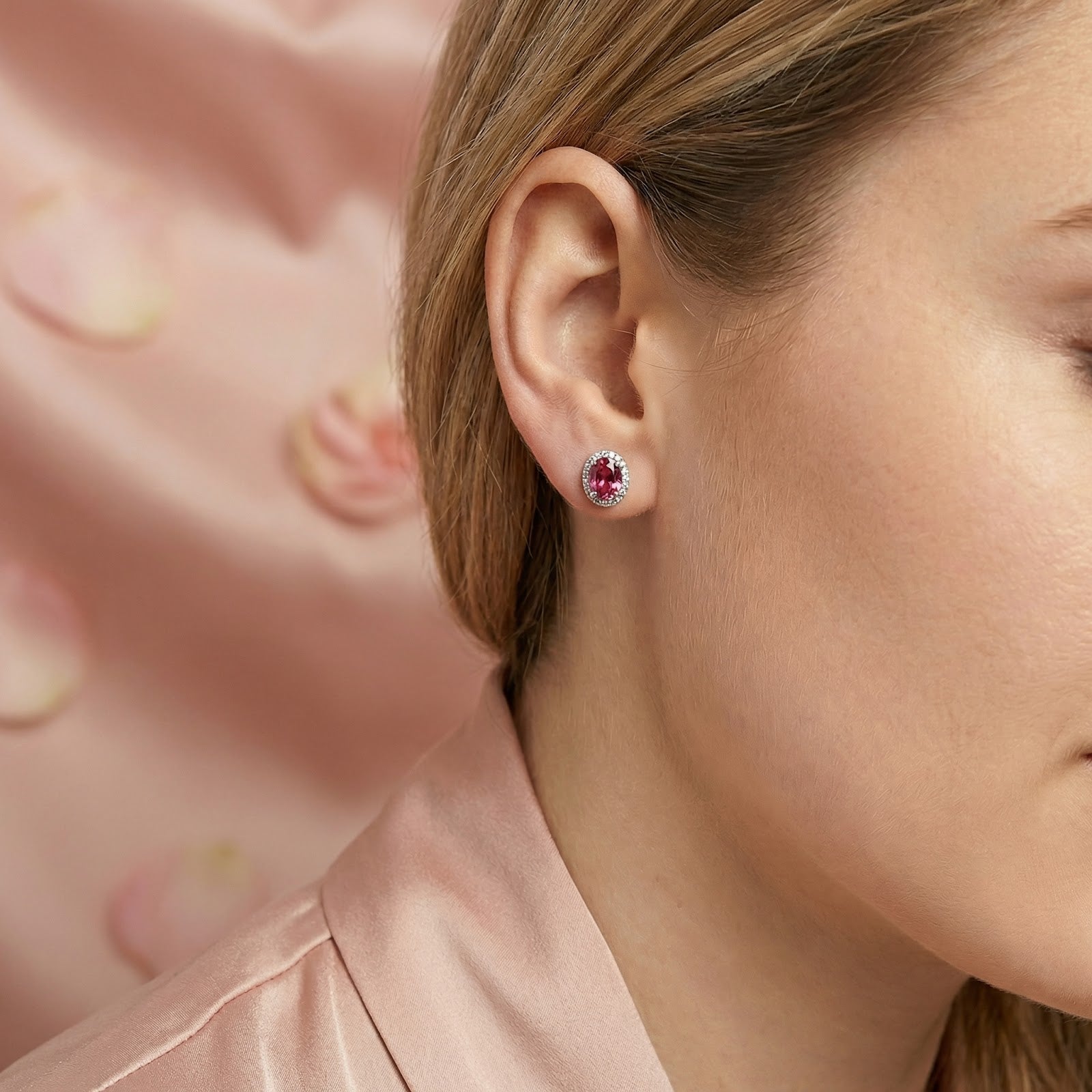 Close-up of a woman wearing an oval-cut pink tourmaline and sterling silver halo stud earring.