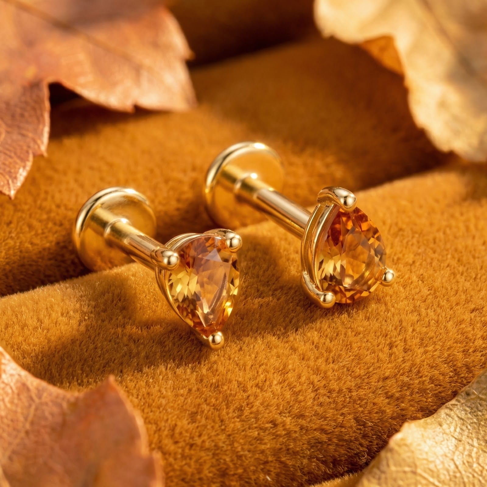 Detail view of pear-cut simulated topaz and 18K gold vermeil stud earrings on velvet with autumn leaves.