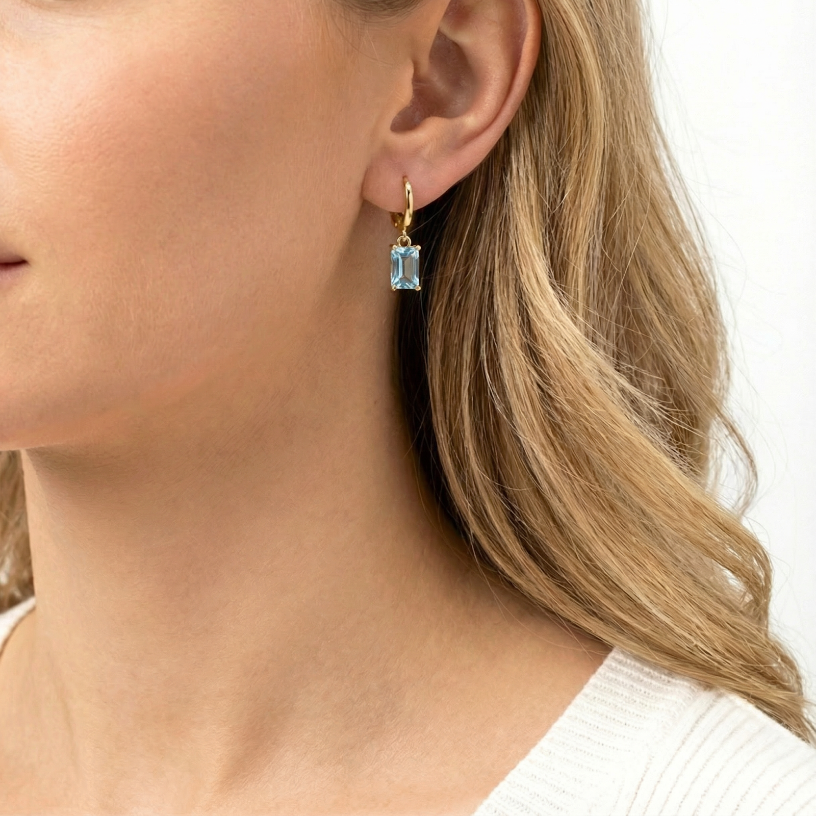 Side profile of a woman wearing 18K gold vermeil hoop earrings with rectangular-cut simulated aquamarine drops.