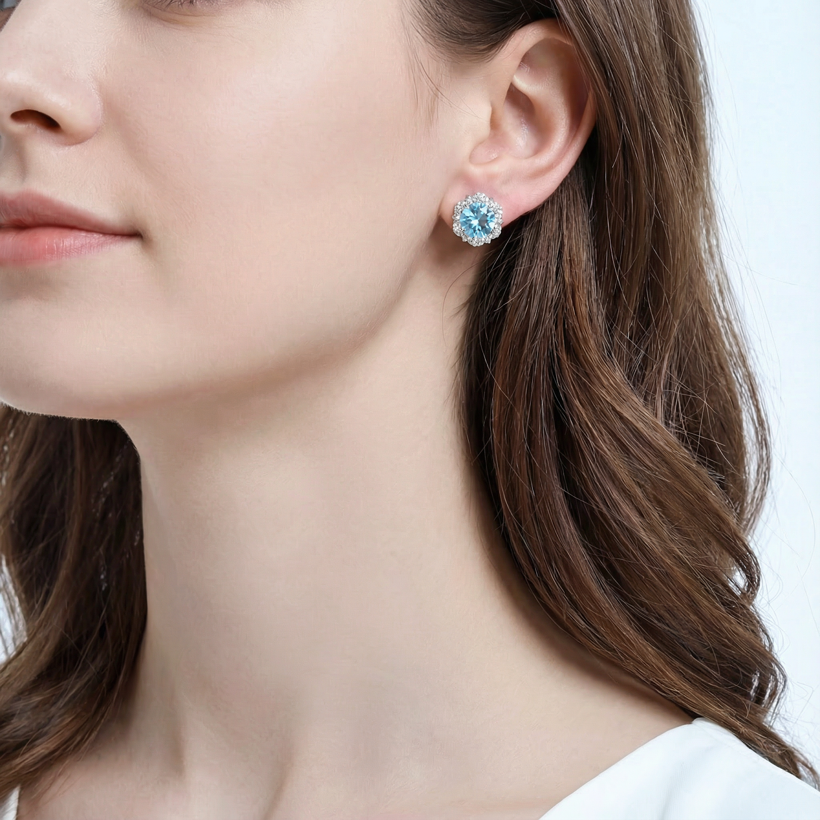 Light blue simulated aquamarine halo stud earring in sterling silver shown on a model's ear.