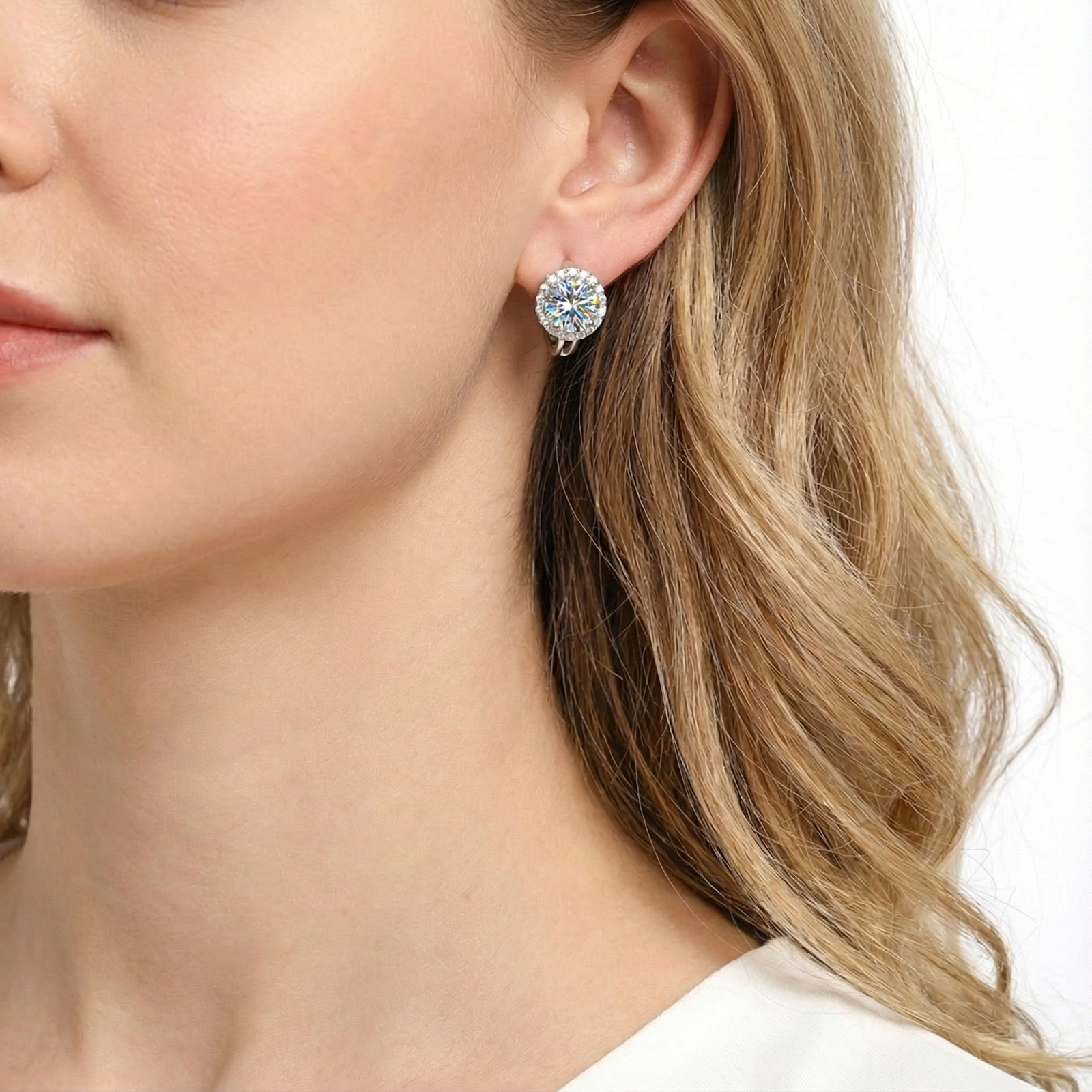Close-up of a brilliant round cut moissanite halo earring in sterling silver worn on a model's ear.