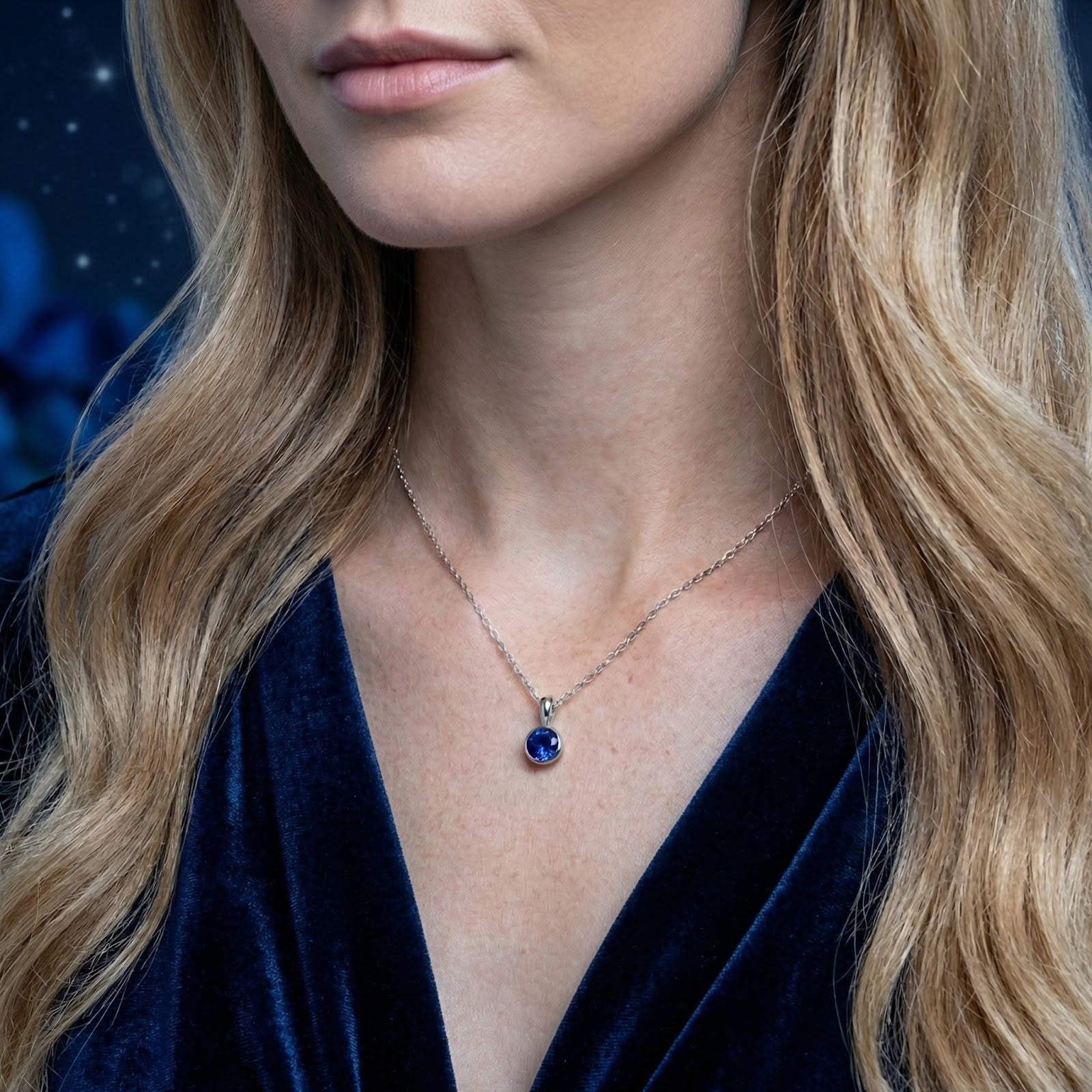 Close-up of a model wearing a sterling silver necklace with a round-cut royal blue simulated sapphire pendant.