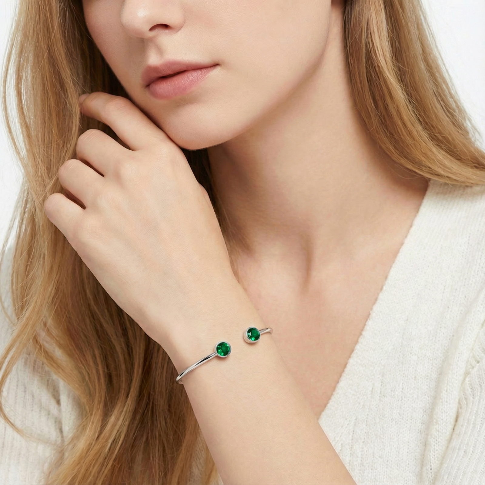 Silver stainless steel bypass cuff bracelet with round simulated emeralds worn on a model's wrist.